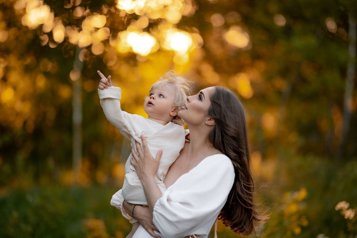 Mother and child playing together against golden bokeh background at sunset.