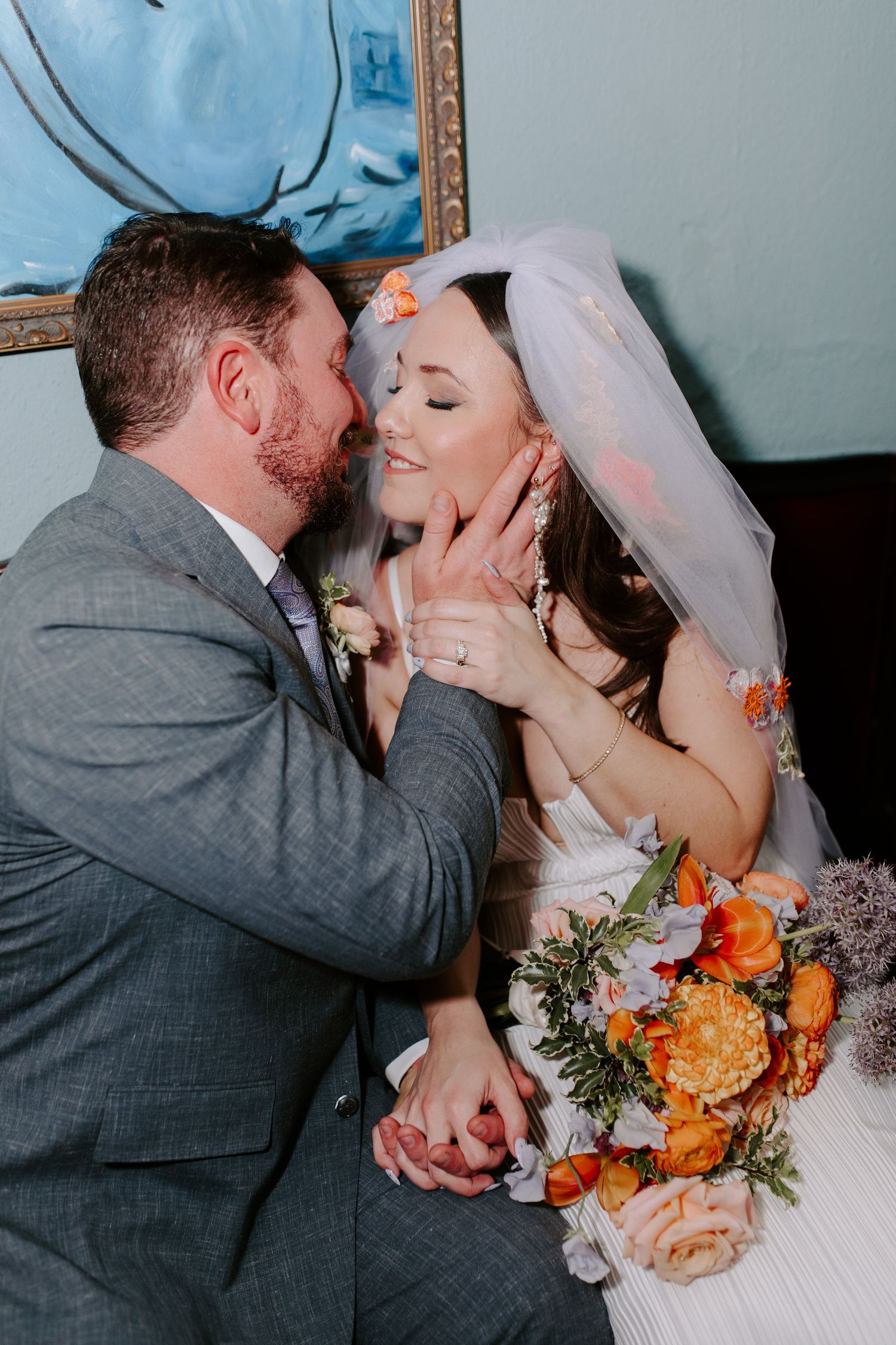 Romantic wedding portrait shows couple sharing an intimate moment with orange bouquet and elegant attire.