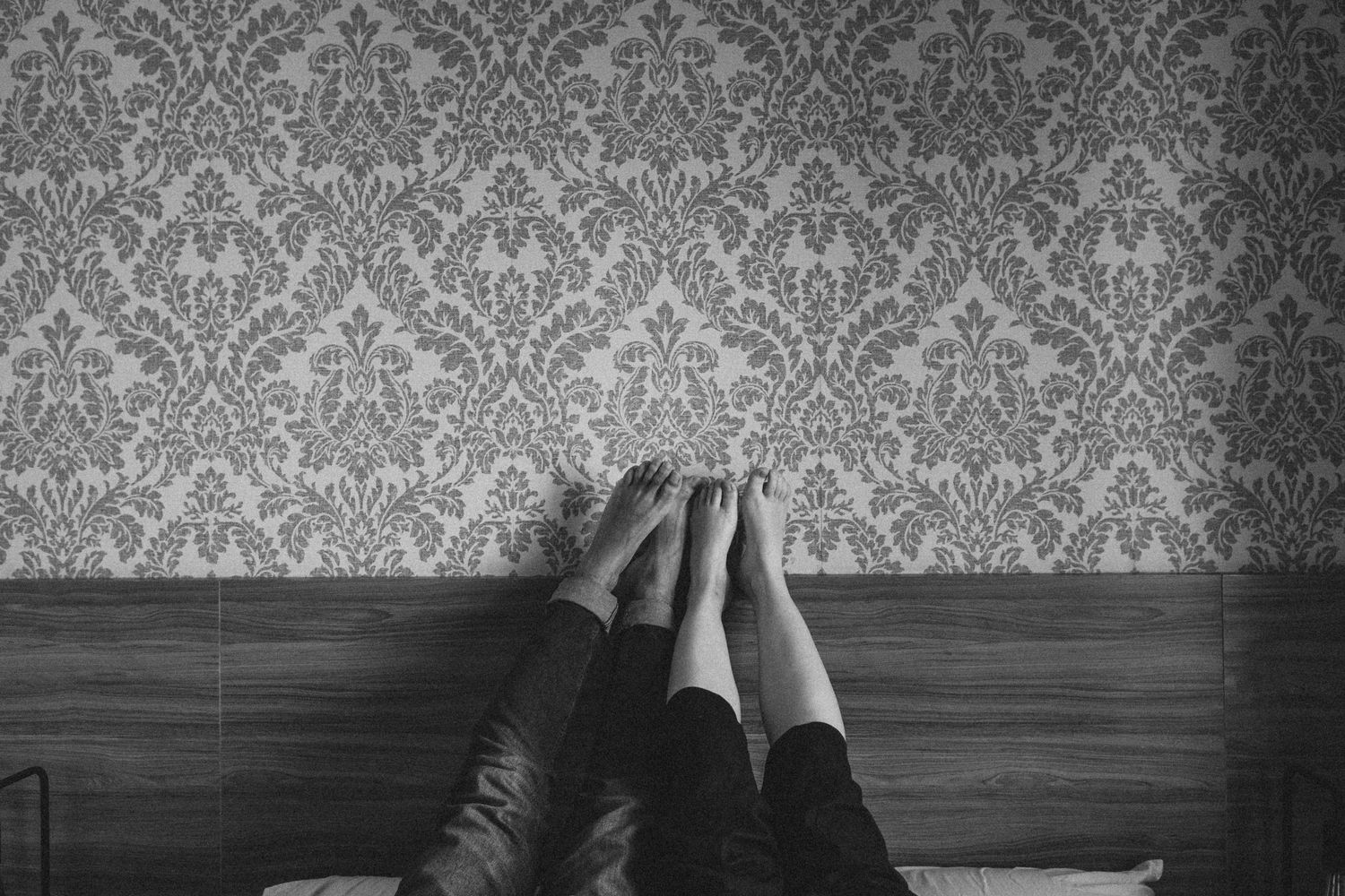 Black and white image of feet against a wallpapered wall.