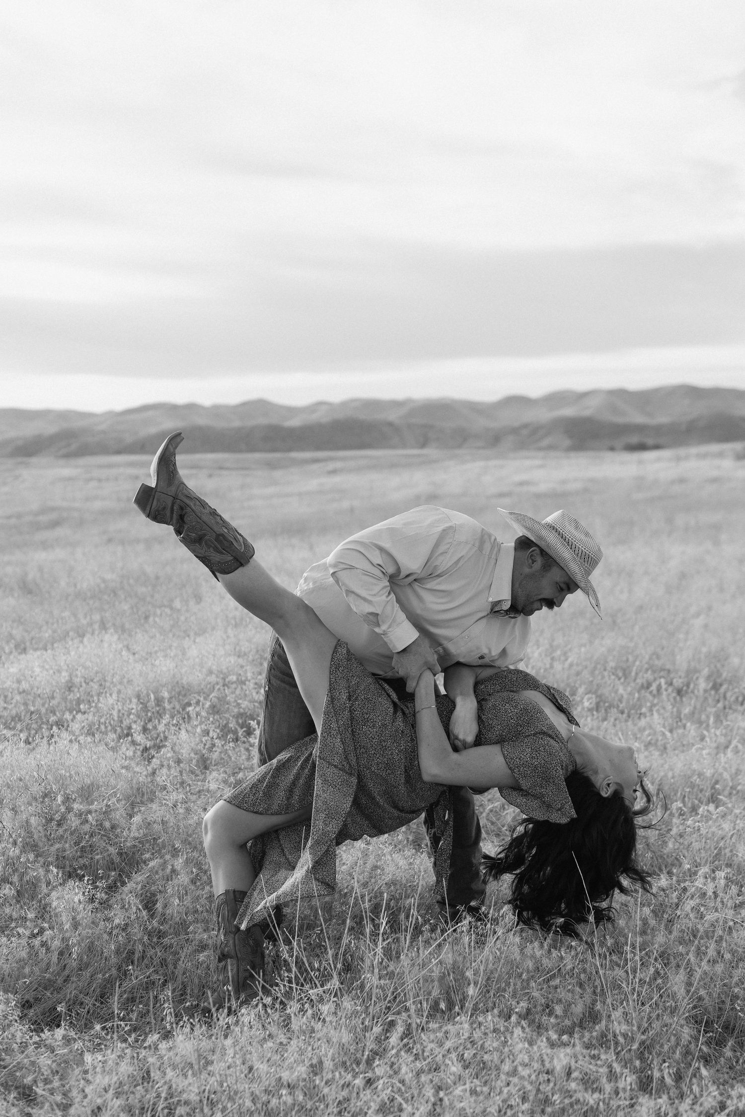 A couple in western wear sharing a playful moment on a blanket outdoors.