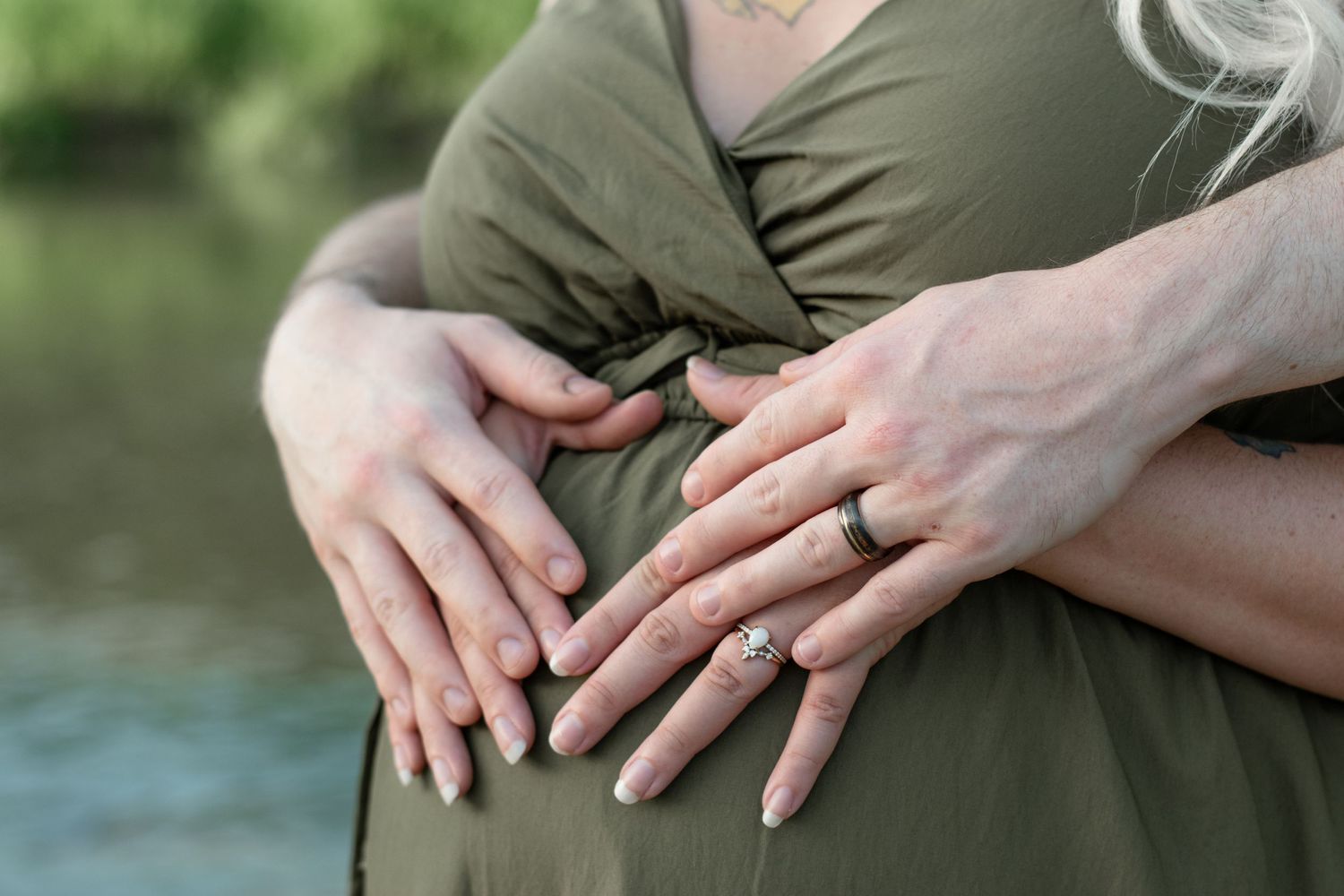 Close-up of hands with engagement rings resting on an olive green dress.
