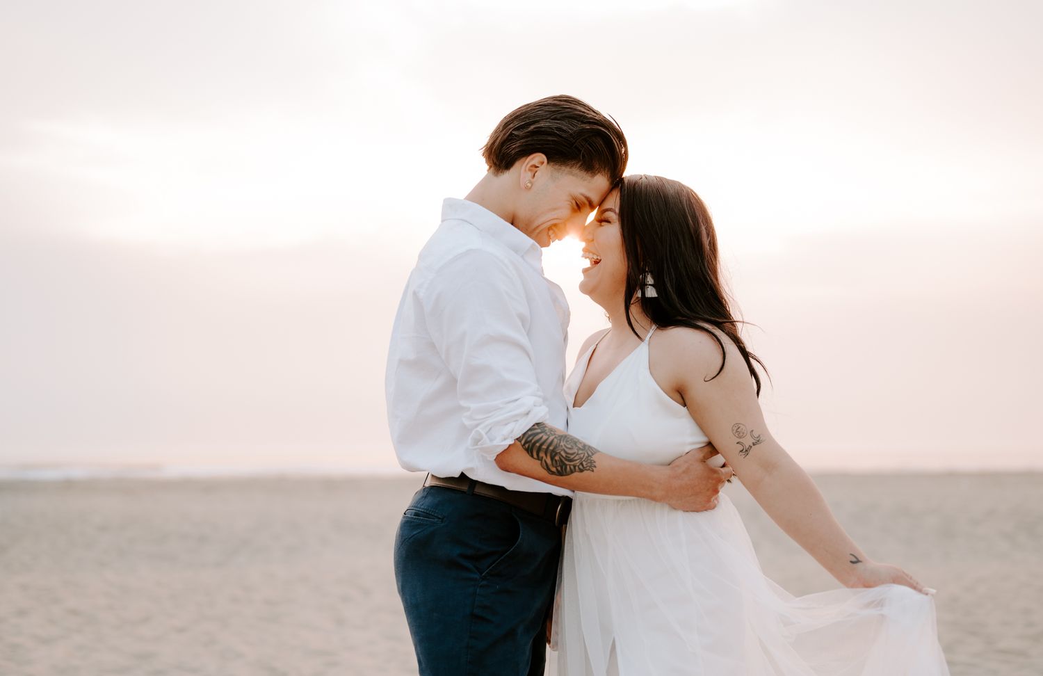 Couple in white clothing sharing a tender embrace on a beach during golden hour.
