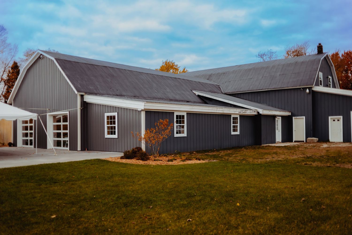 Modern grey barn-style building with white trim and multiple garage doors under blue skies.