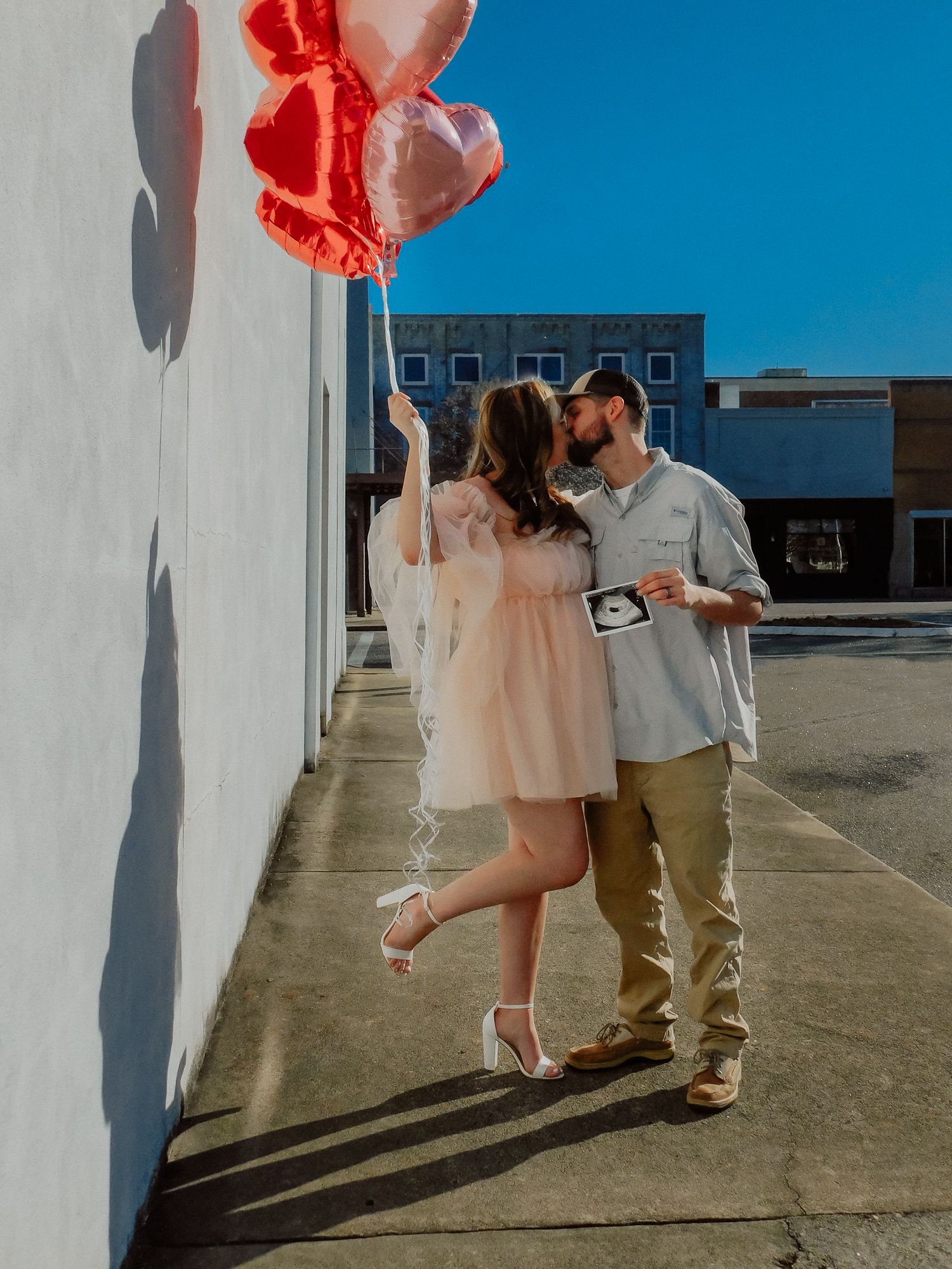 A couple poses in downtown Rockingham, NC with balloons and an ultrasound to announce their new pregnancy with Miranda Jo Photography