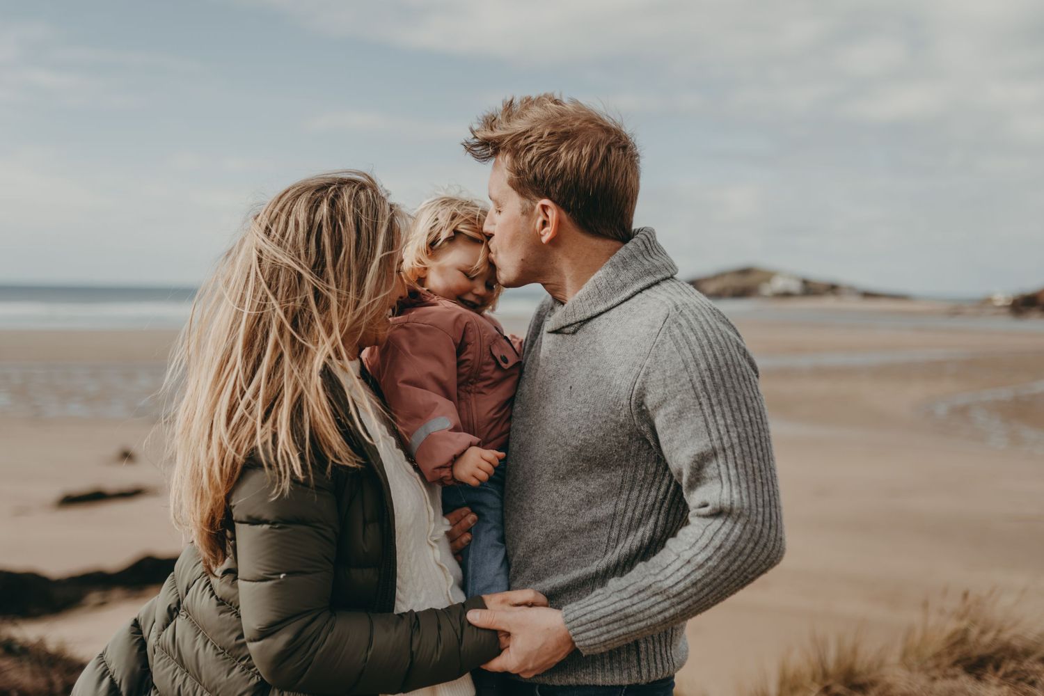 Intimate family moment captured on a windswept beach with ocean views.