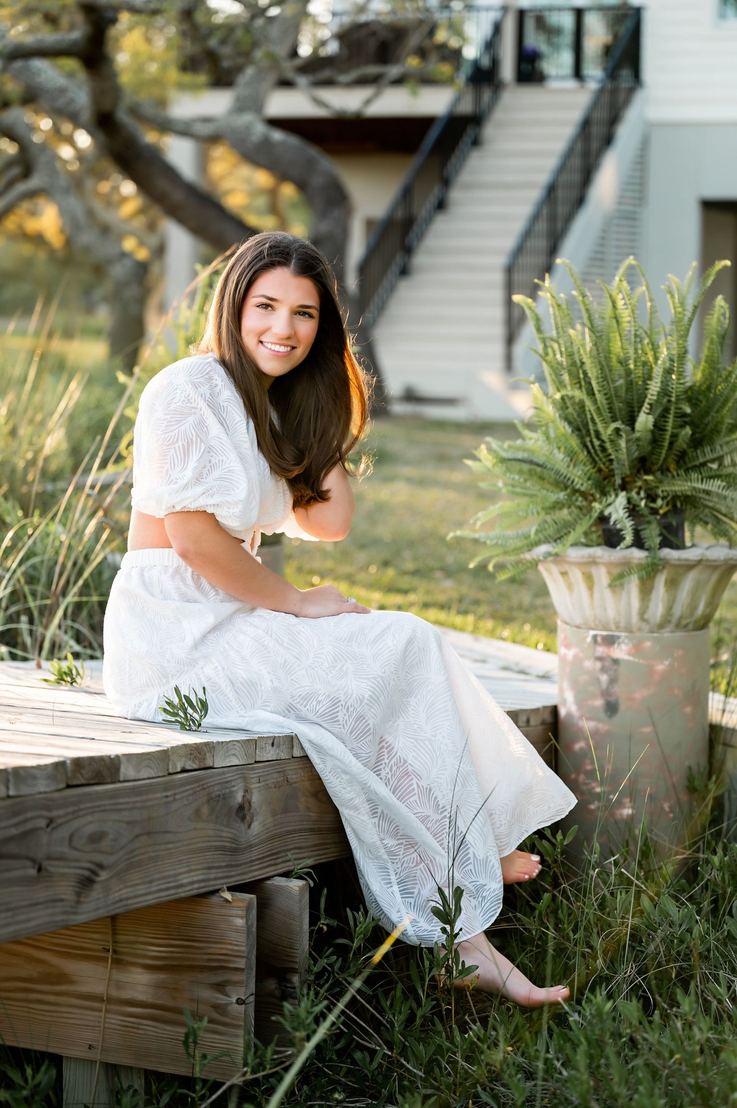 Person in white lace dress sitting on wooden steps near potted plants.