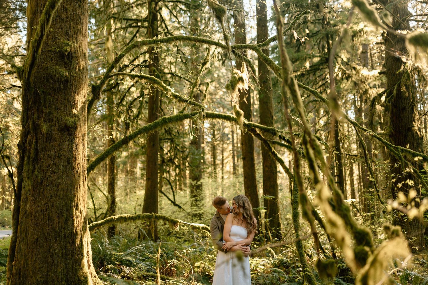 A photograph of an engaged couple in the middle of a mossy forest at Bunzten Lake, Port Moody