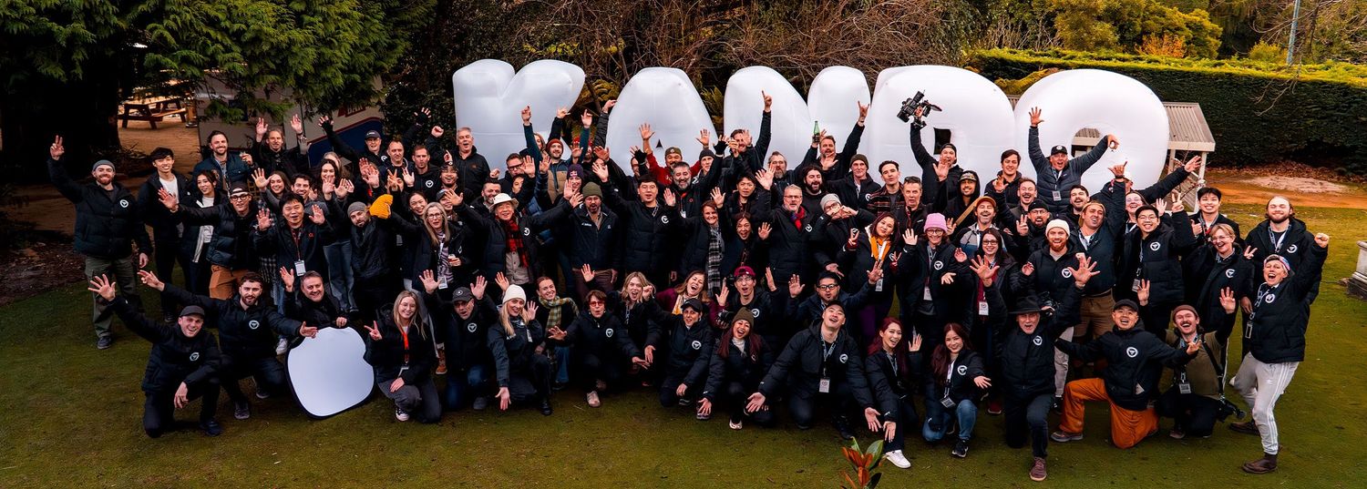 A large group of Sony photographers stand in front of a blow up sign that reads KANDO