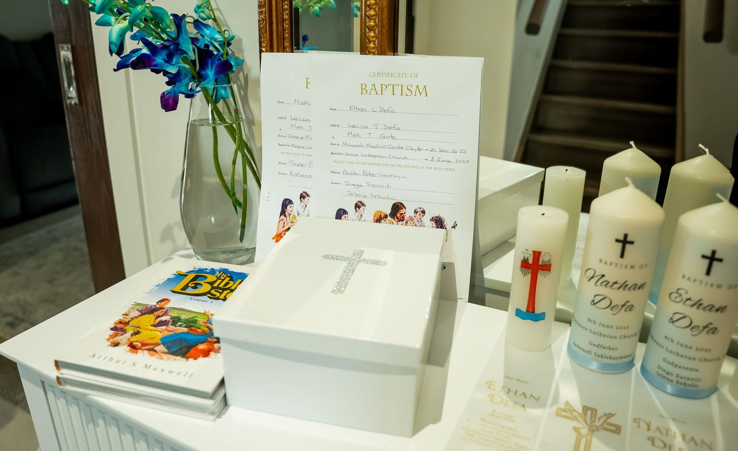 Baptism ceremony display with white candles, blue flowers and religious items arranged on a table.