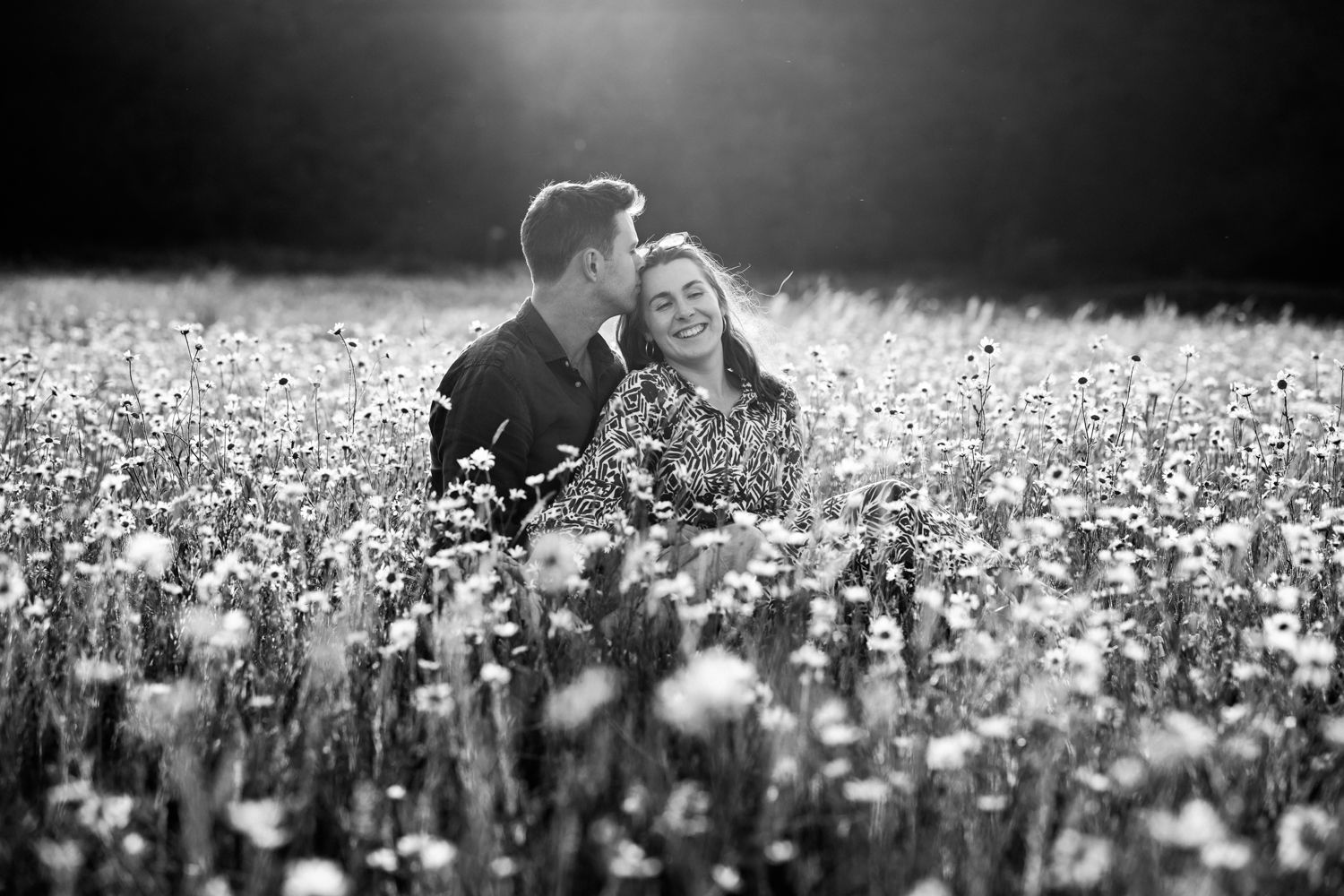 A romantic black and white photograph of a couple sitting together in a blooming field of wildflowers.