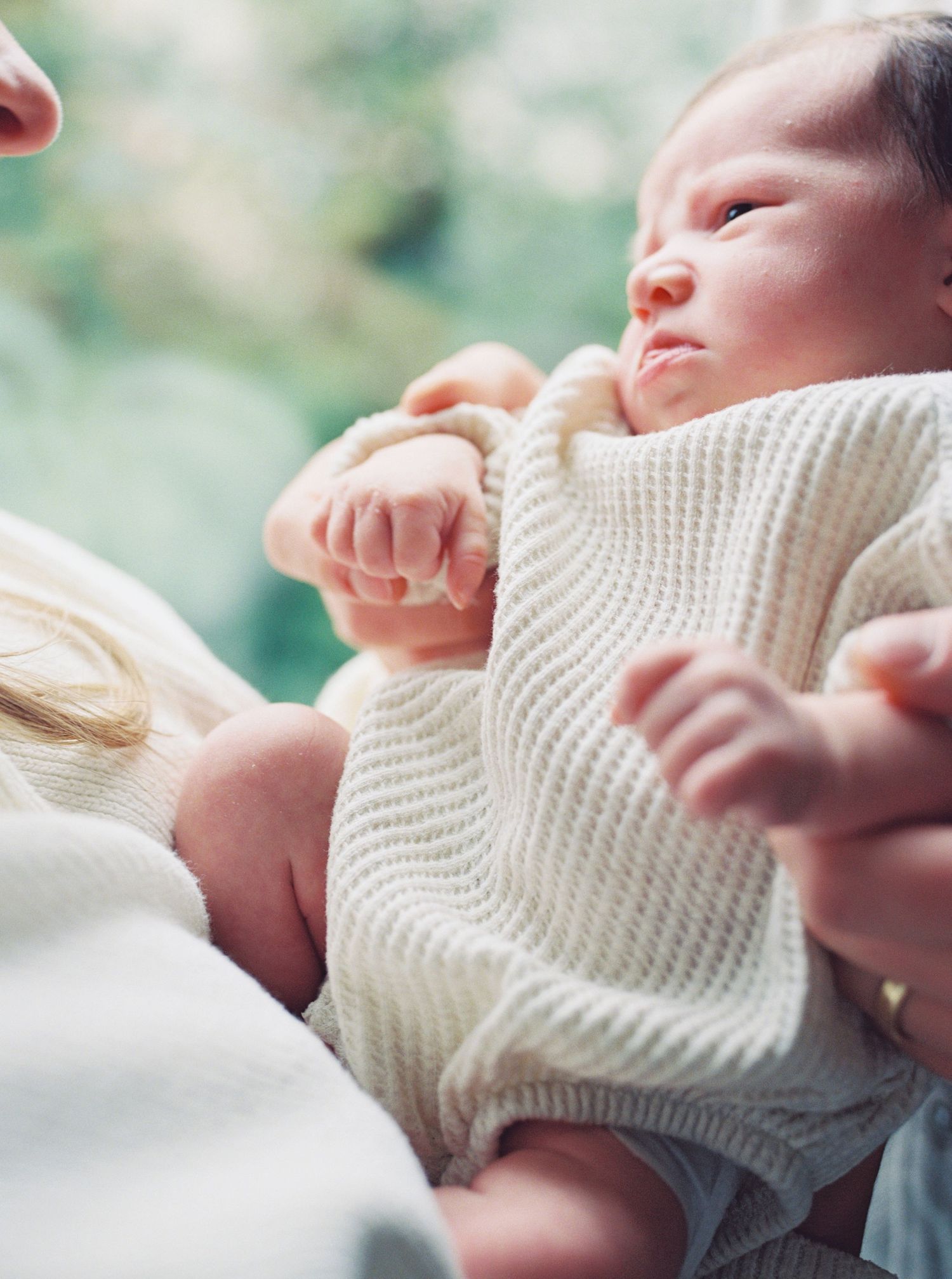 A newborn baby wearing a cozy white knit sweater stretches their tiny arms while resting peacefully.