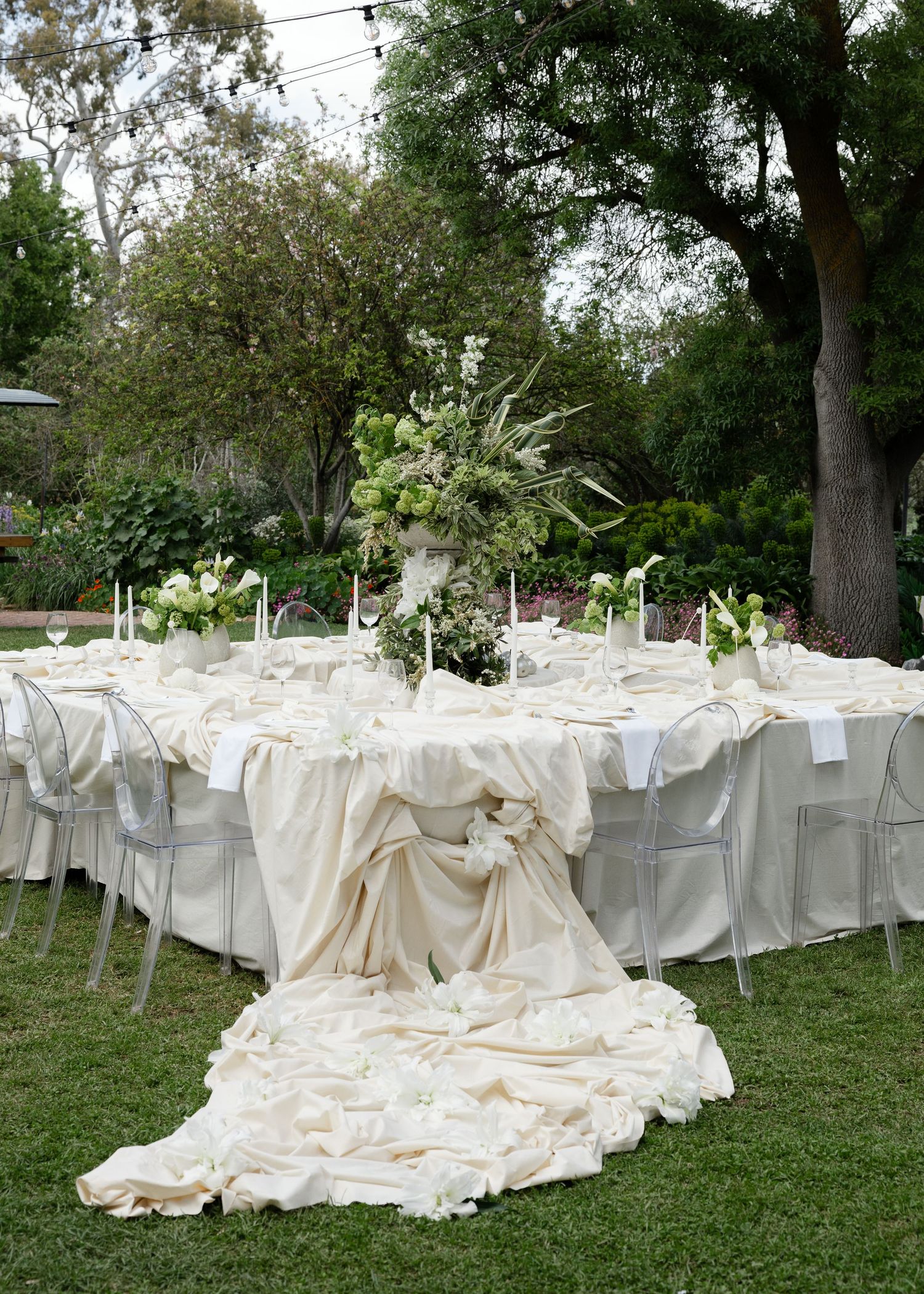 Rows of white-draped dining tables and chairs set up outdoors for an elegant garden wedding reception.