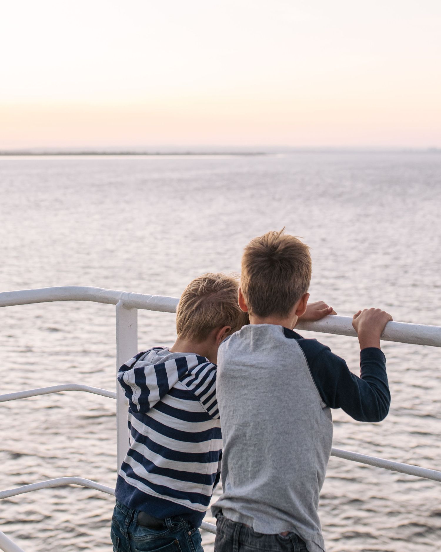 Two children leaning on railing overlooking ocean at sunset.
