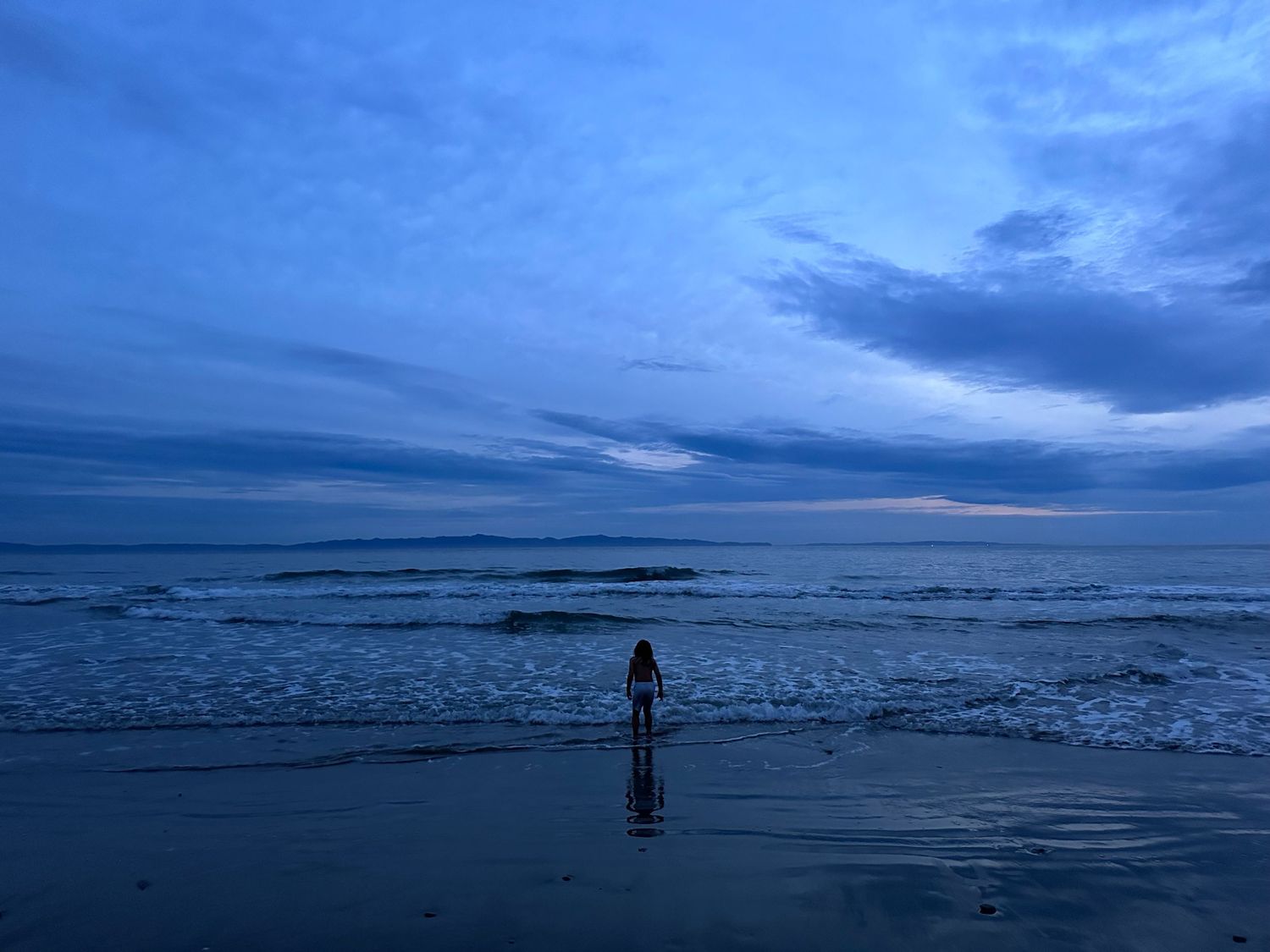 Dramatic sequence of ocean waves and stormy skies at dusk with silhouetted figures on the beach.