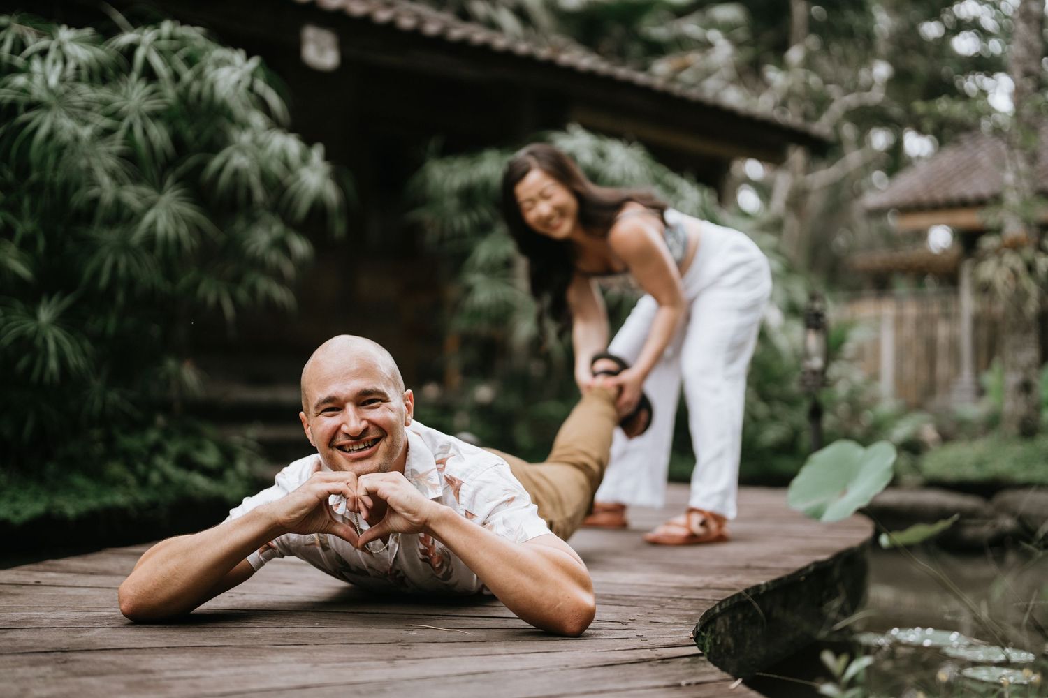 Couple strolling through verdant tropical garden pathway with traditional Balinese architecture.