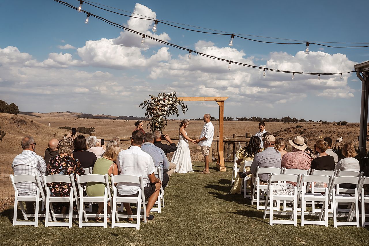 An outdoor wedding ceremony setup features rows of white folding chairs overlooking a scenic countryside landscape.