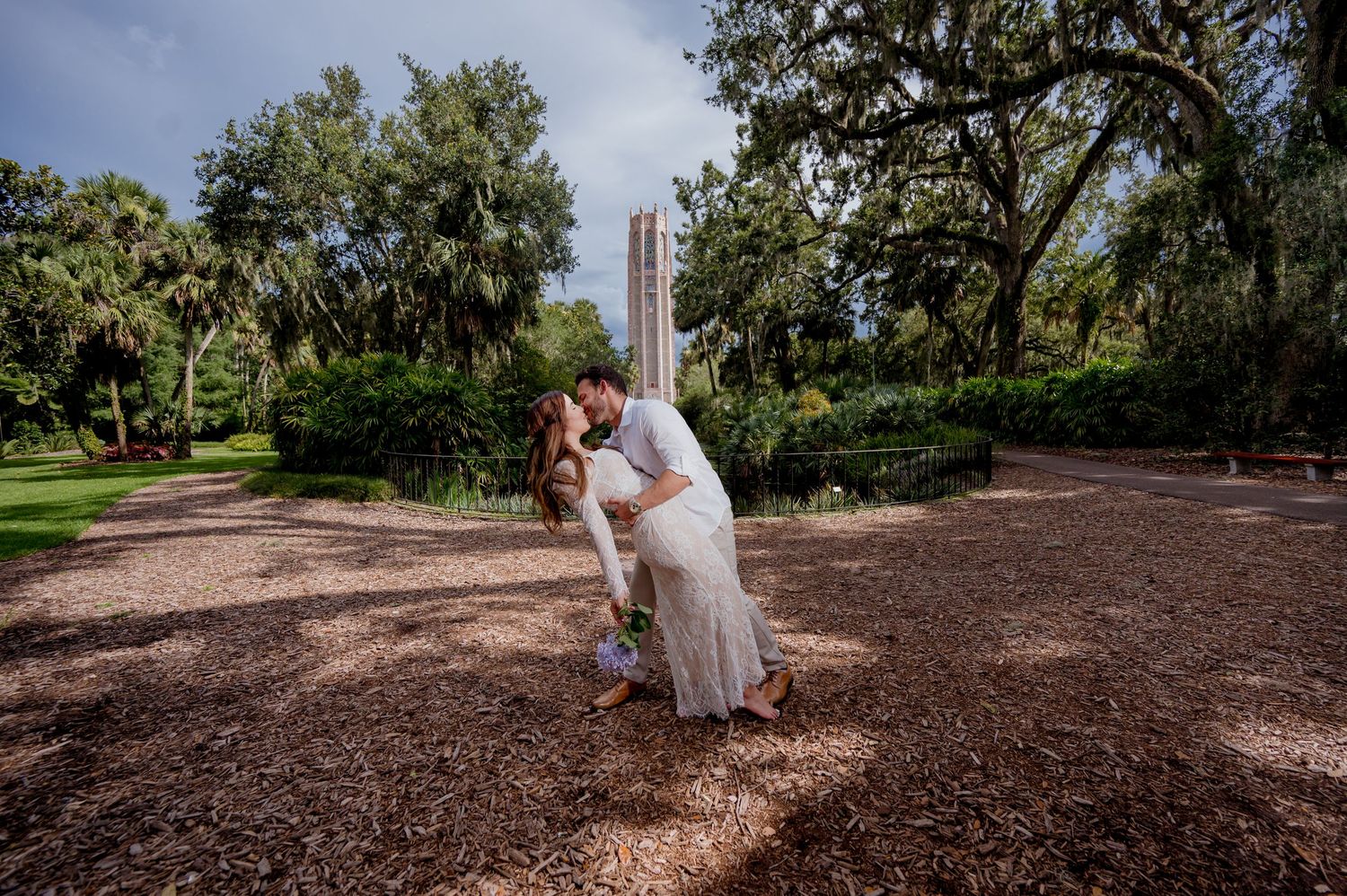 A couple in wedding attire embrace under spanish moss and oak trees at Bok Tower Gardens in Florida.