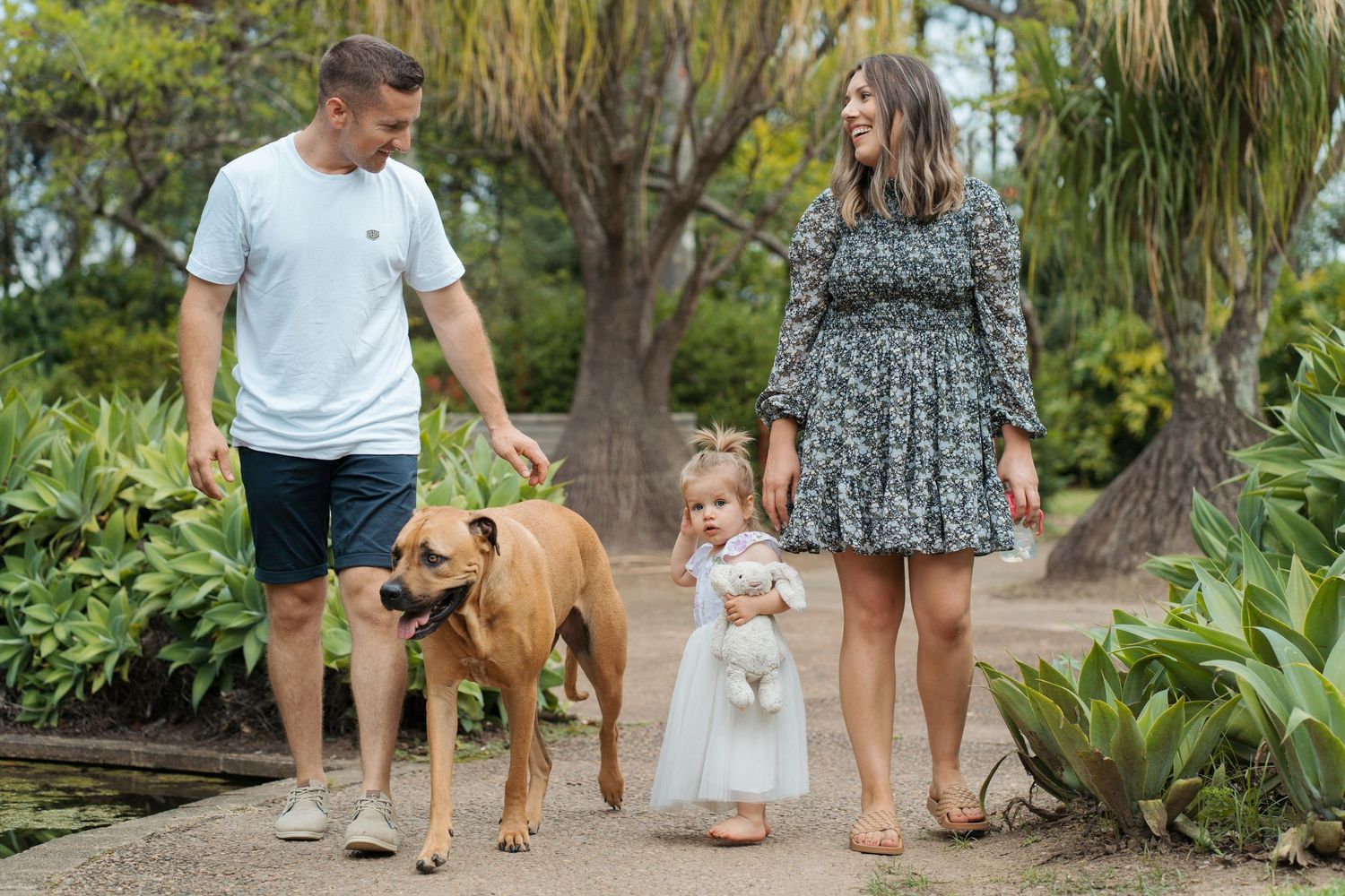 A family walks together with their dogs through a lush garden path on a gloomy day family photoshoot in Fagan Park Sydney