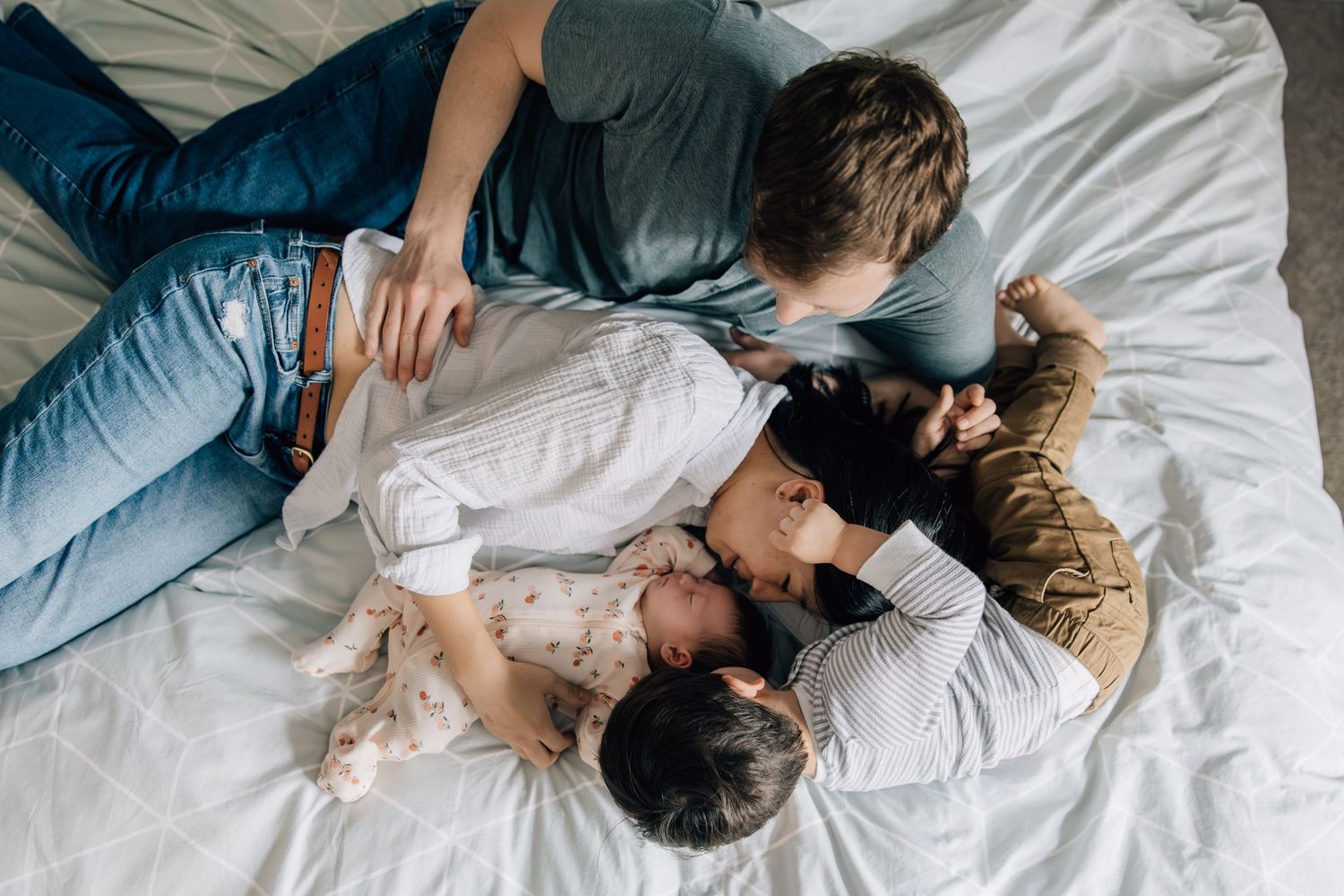 Overhead view of a family cuddling together on a white bed with their newborn baby.