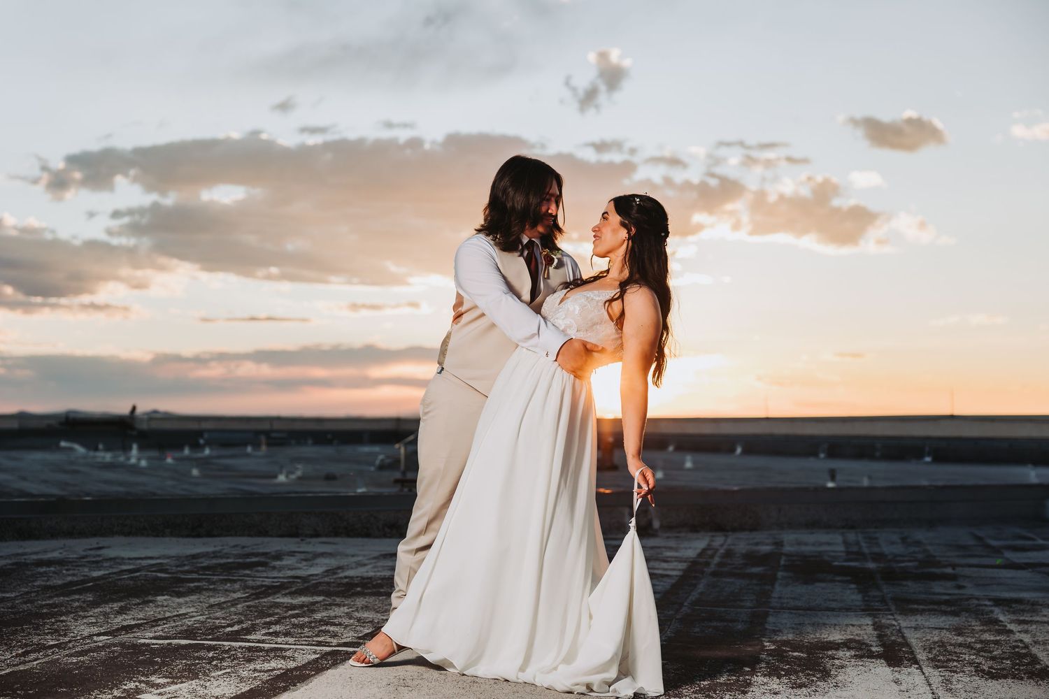 A couple in white outfits share an intimate moment at sunset on a beach with dramatic clouds in the background.