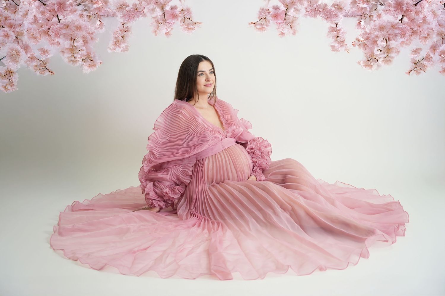 A flowing pink pleated gown with cascading ruffles twirls elegantly in a bright studio setting.