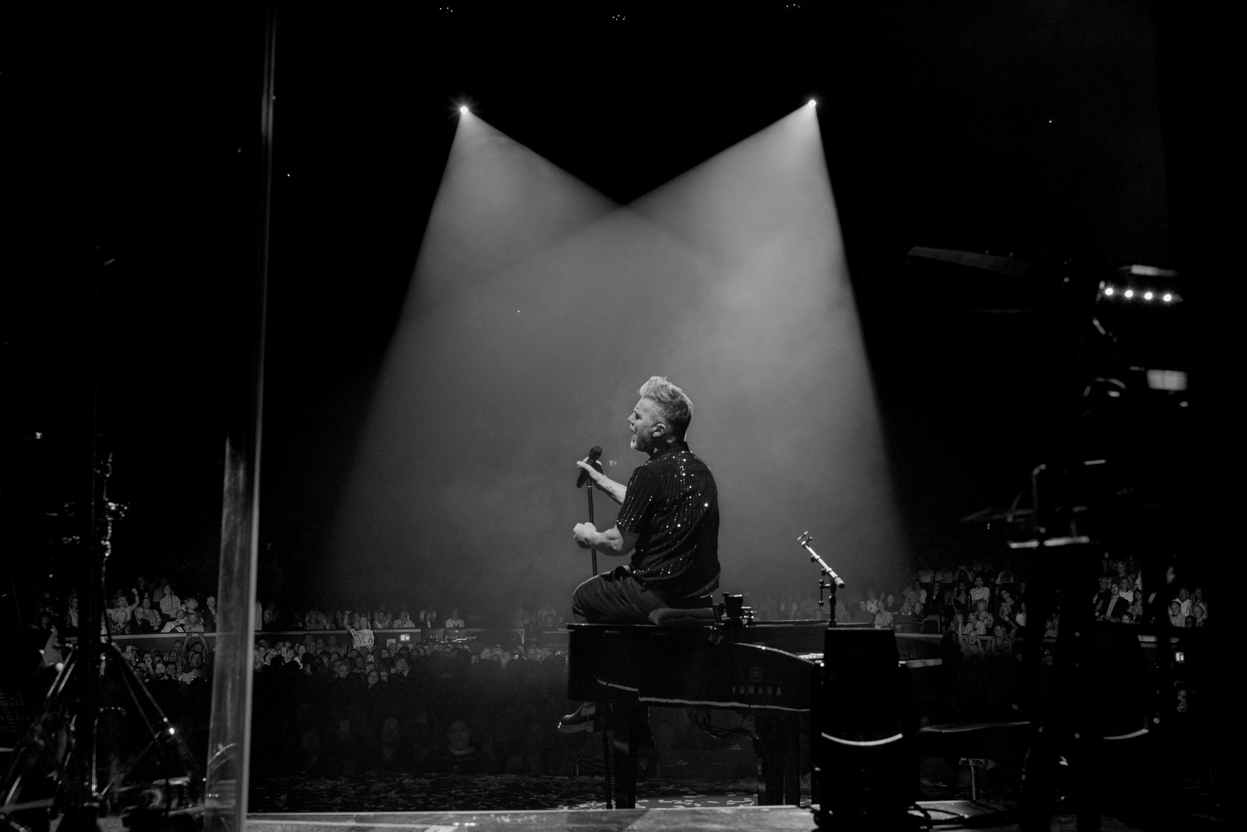A musician performs on stage, illuminated by a dramatic spotlight in a black-and-white concert photograph.