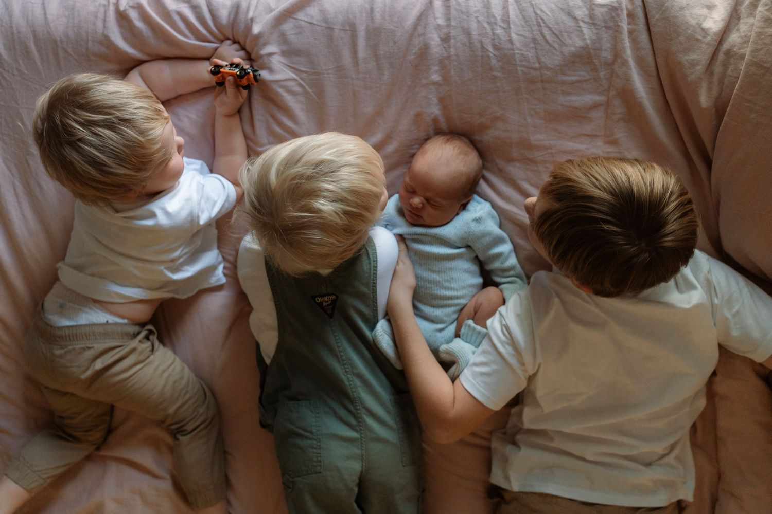Children snuggle together on a beige couch wearing casual clothes in an overhead view.