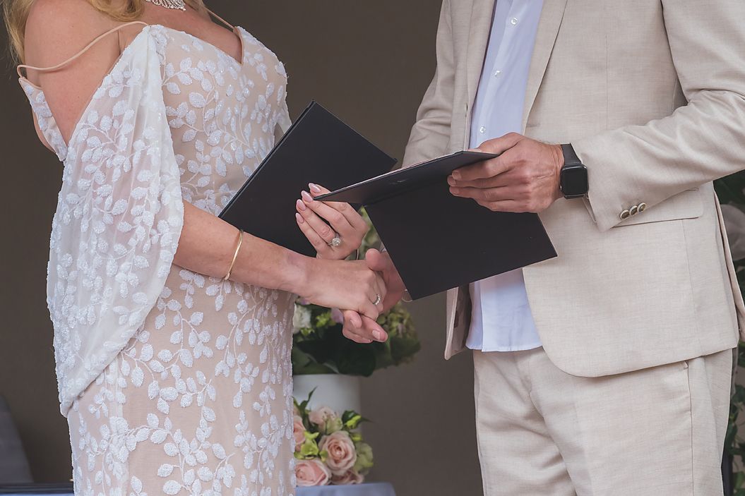 A close-up of hands holding a book during an outdoor wedding ceremony as vows are exchanged.