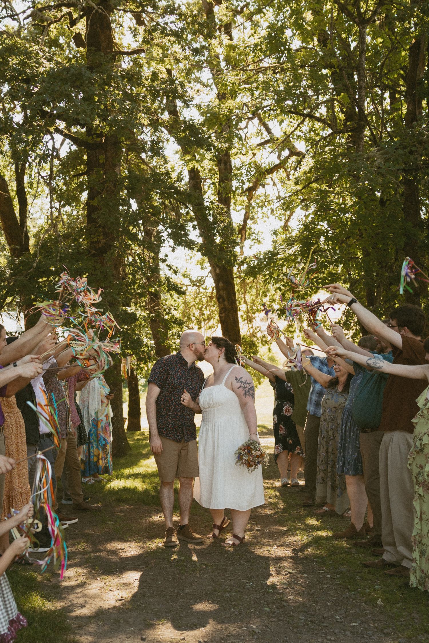 Wedding guests form an archway with raised arms as newlyweds walk beneath.