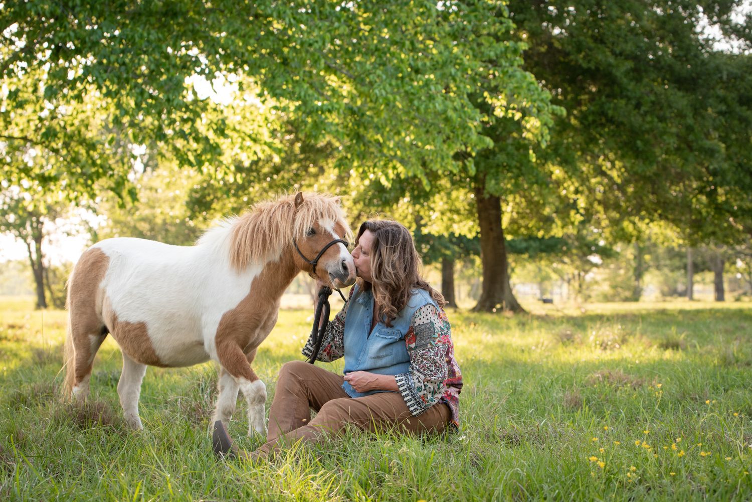 Woman gently leaning forehead to horse during equine photo session at golden hour.