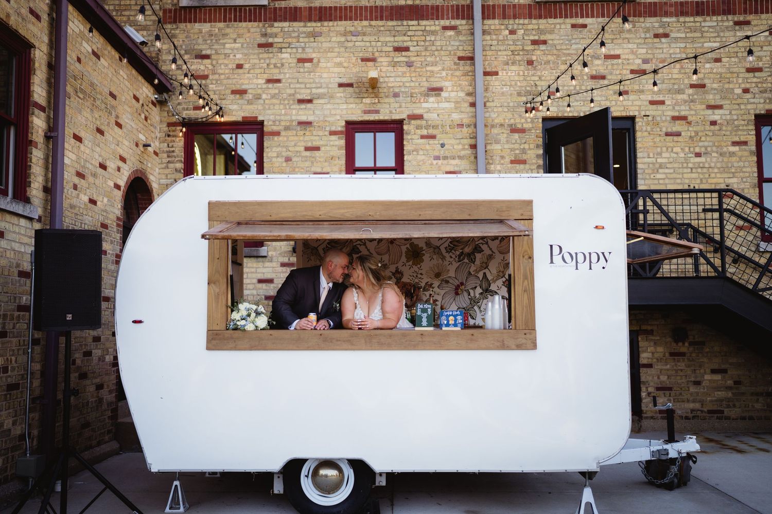 Vintage white camper trailer parked in front of rustic brick building with window displays.