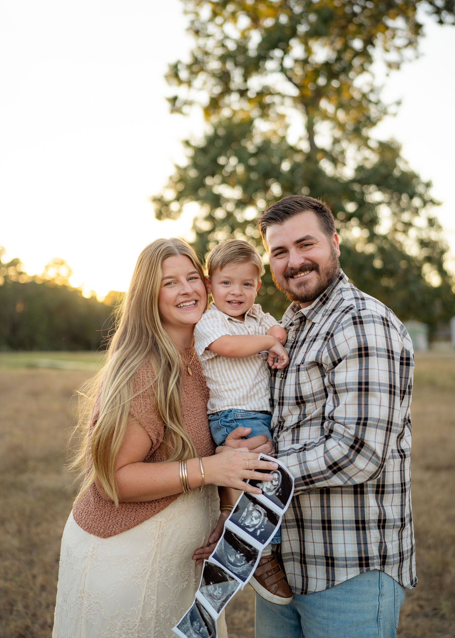 Playful family photo of parents holding their toddler while celebrating baby #2 on the way.