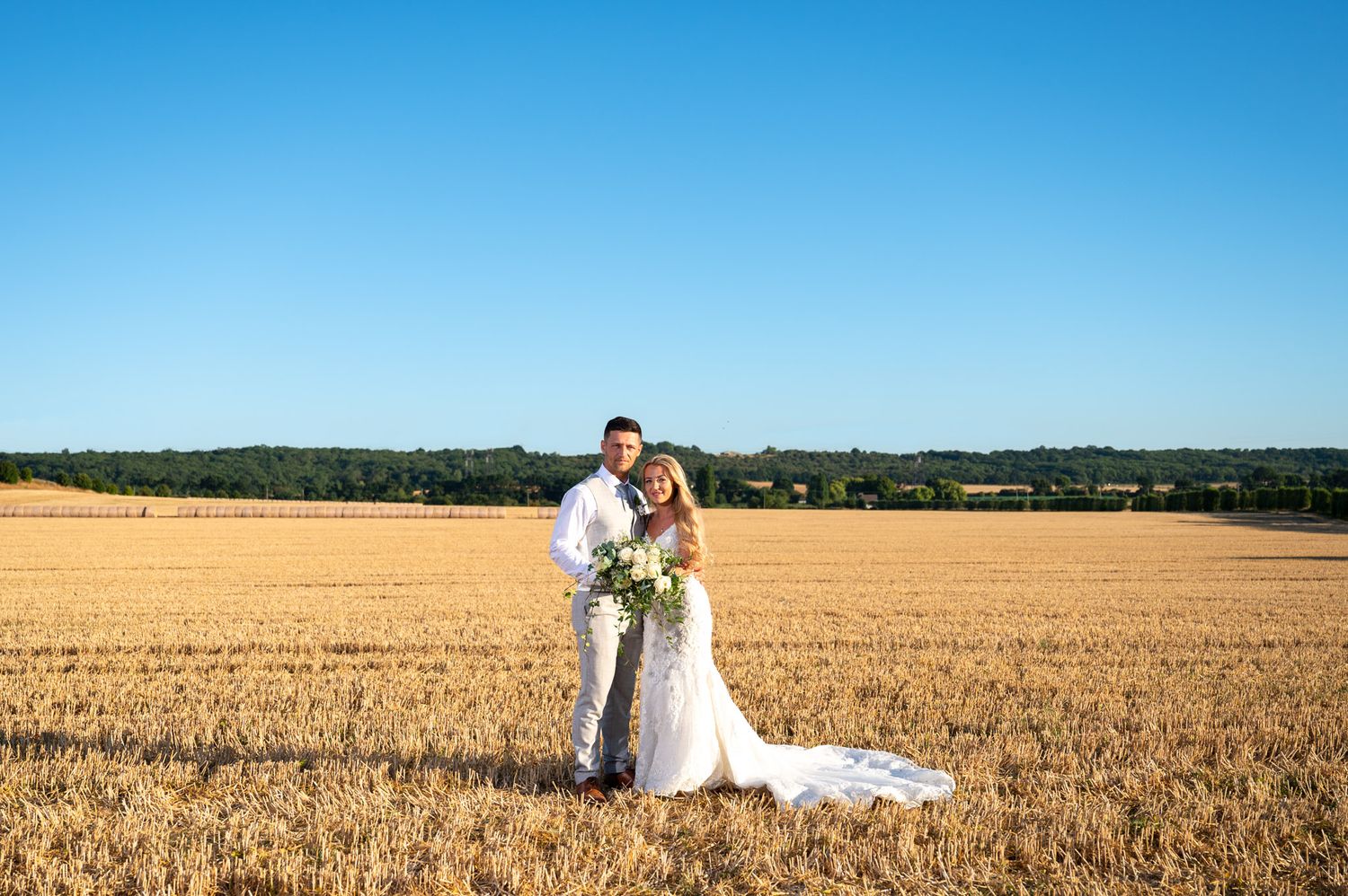 A couple shares a romantic moment in a golden wheat field during a wedding photoshoot on a sunny day.