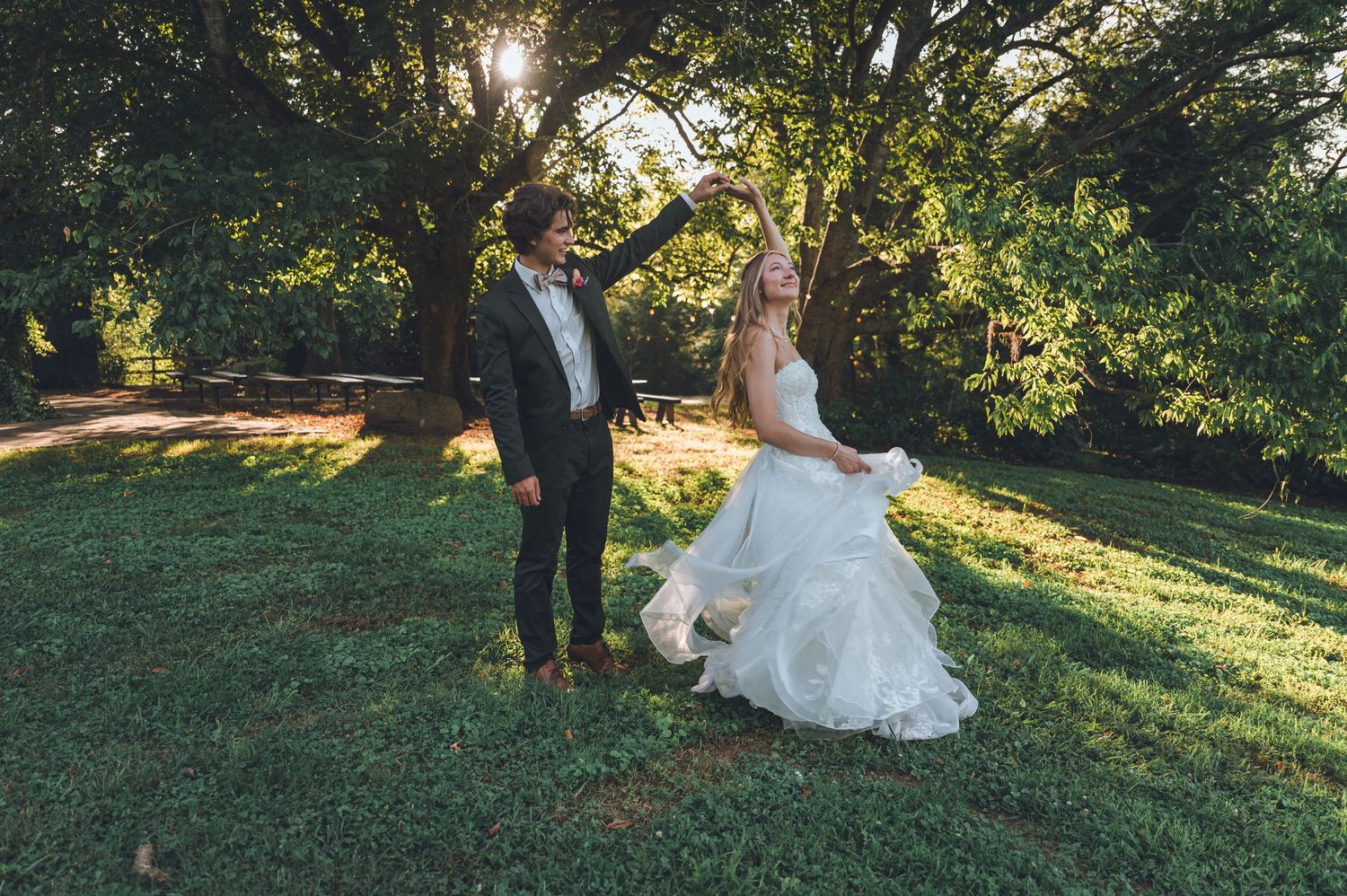 A couple in wedding attire poses in a sunlit garden setting during golden hour at sunset.