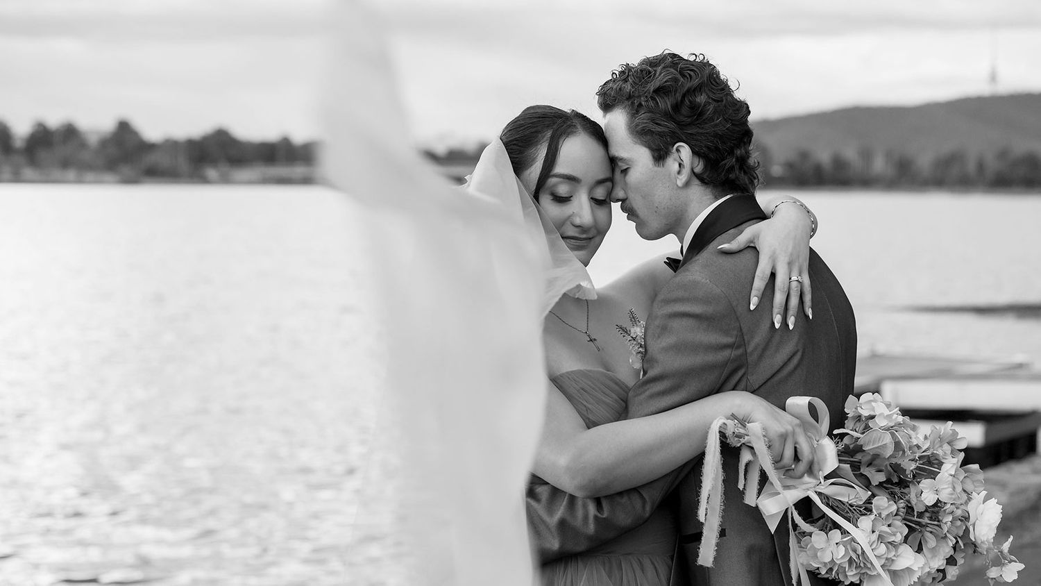 Black and white image of a bride and groom sharing a hug at the Boat House Canberra with Telecom tower in the background.