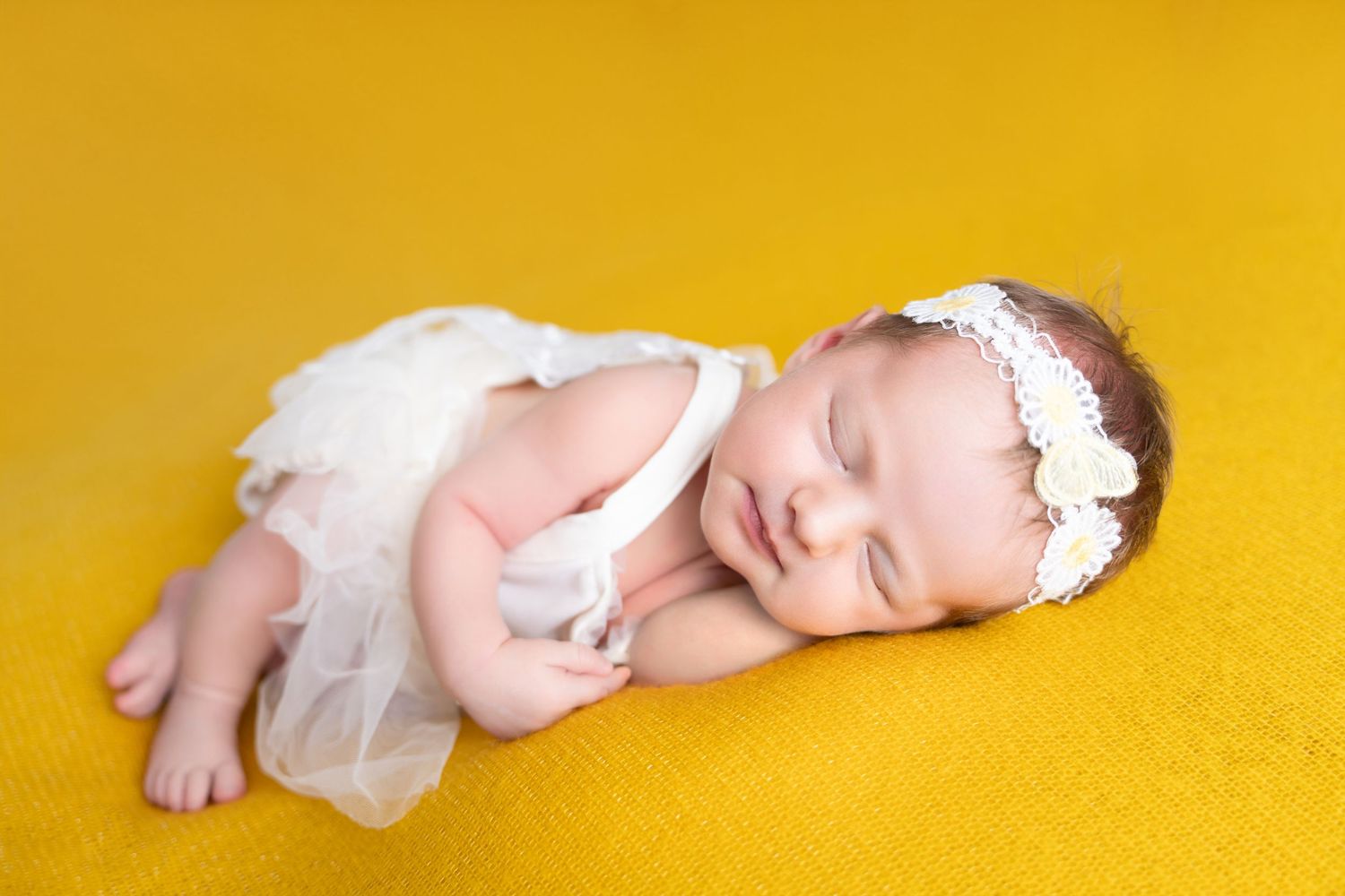 Adorable sleeping newborn baby lying on bright yellow background wearing white onesie.