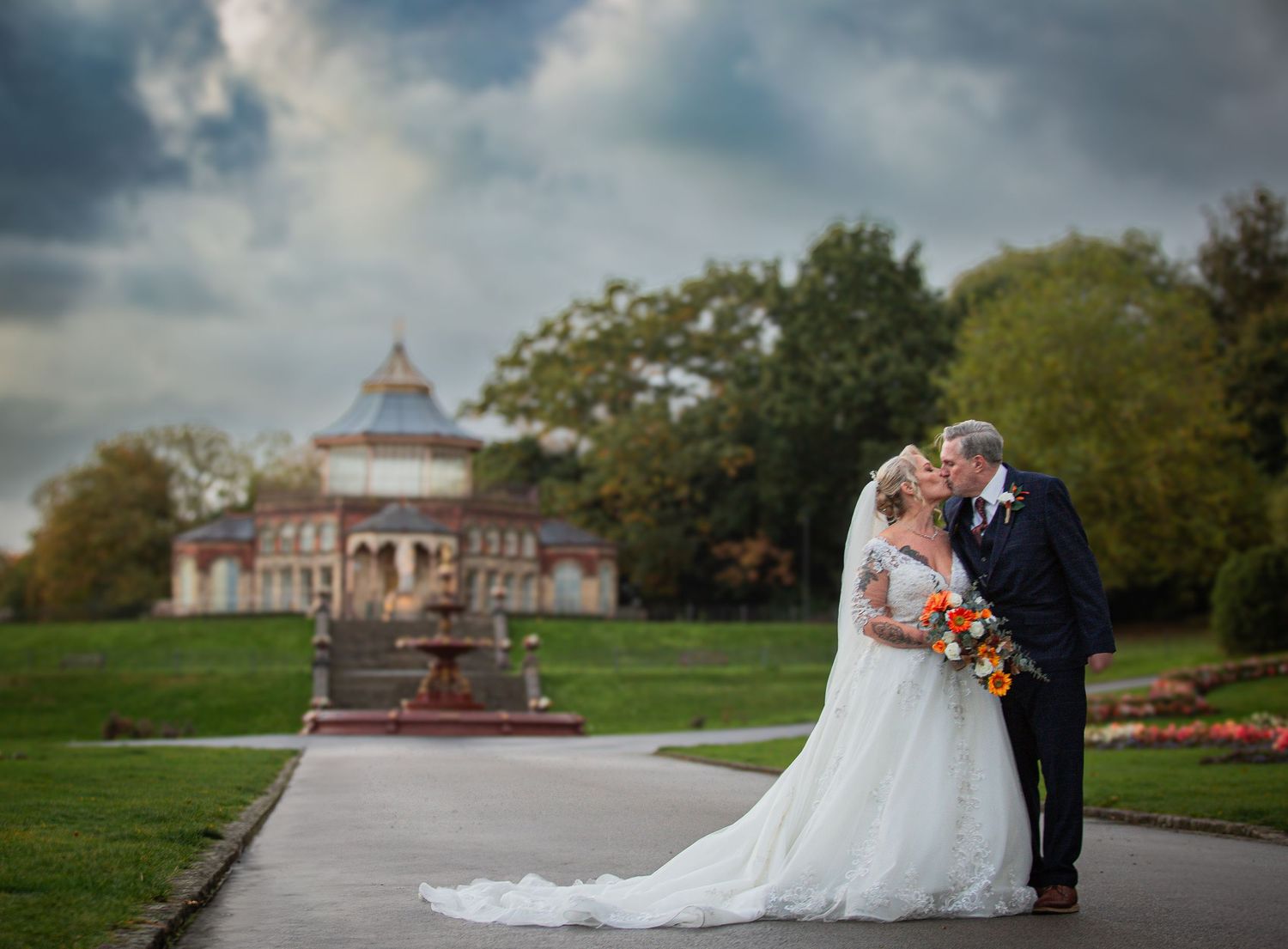 A wedding couple poses at different scenic outdoor locations in a beautiful park setting with historic buildings and autumn colors.