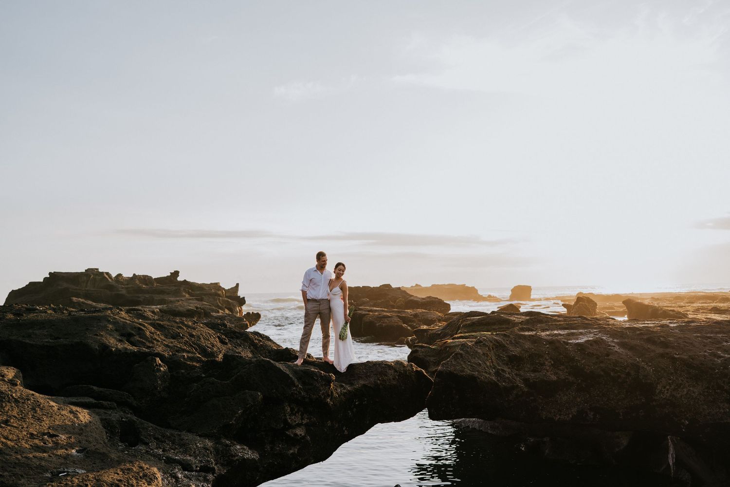 A couple explores rocky coastal cliffs during a dramatic sunset photoshoot.