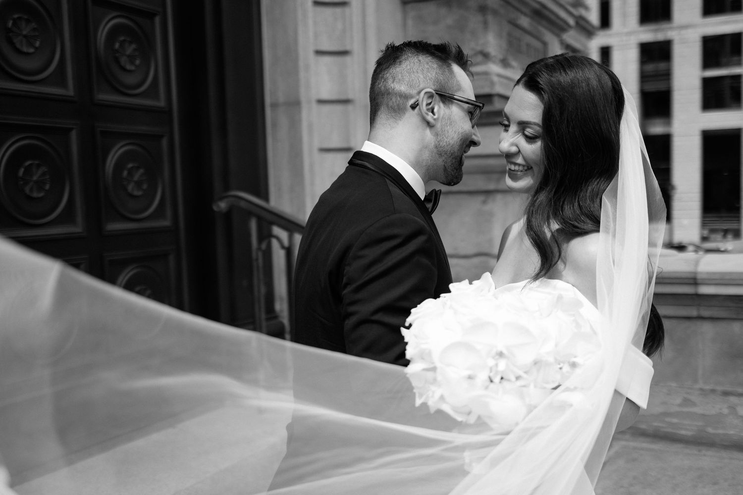 Black and white wedding photo of bride and groom sharing an intimate moment, veil flowing in the wind.
