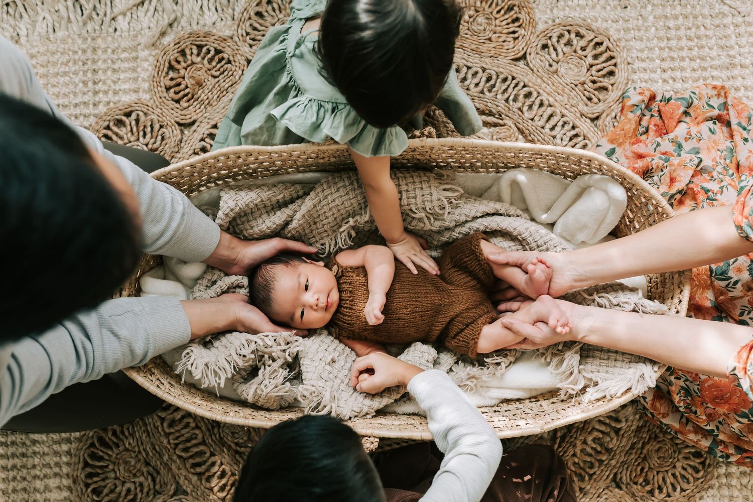 Hands gently surrounding a baby in a wicker cradle.