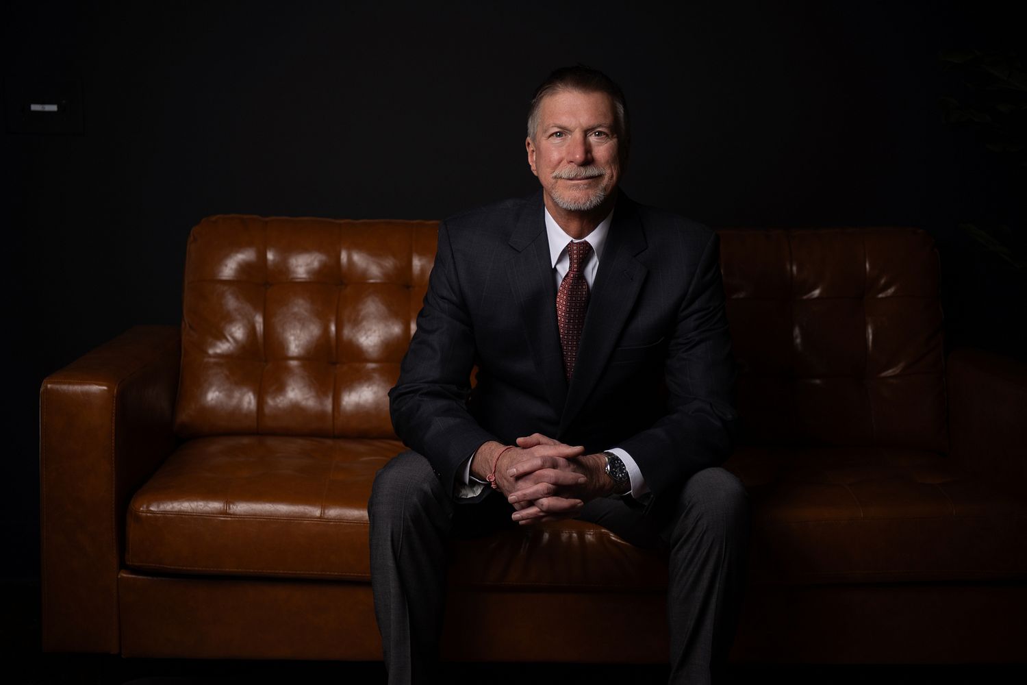 Professional portrait series showing a person in a dark suit against a brown leather couch in dramatic lighting.