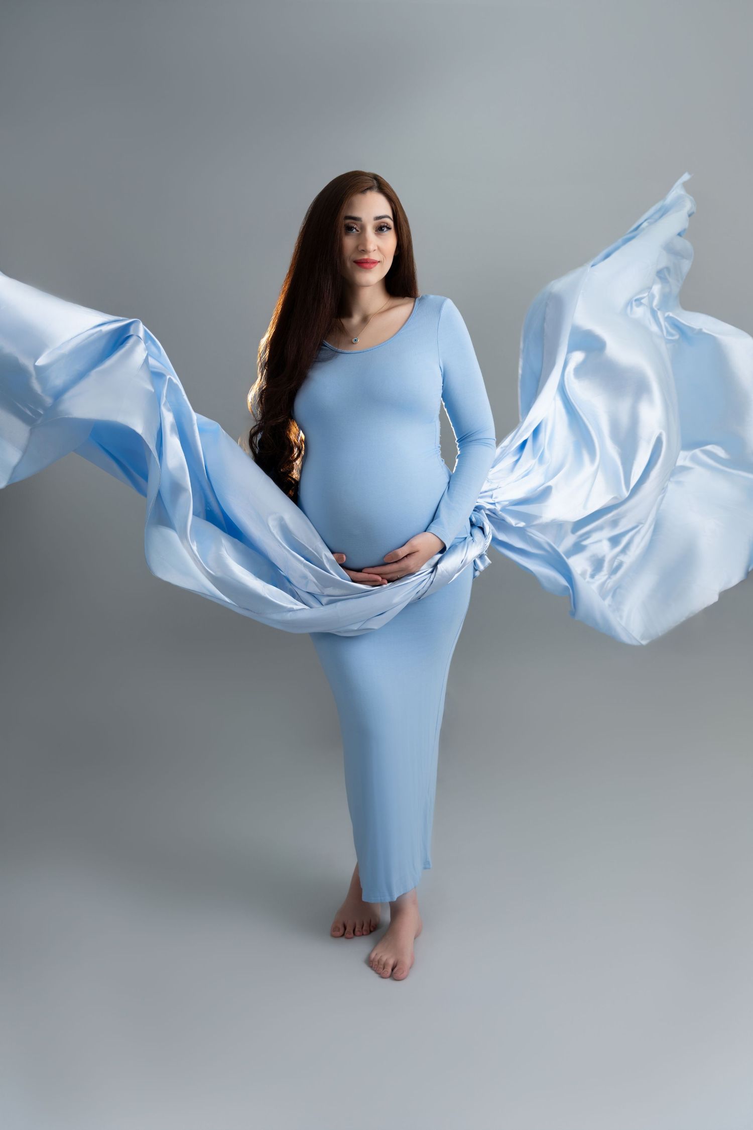 Pregnant woman in flowing gown posing on the golden dunes of Al Qudra and Mleiha during a maternity photoshoot in Dubai.