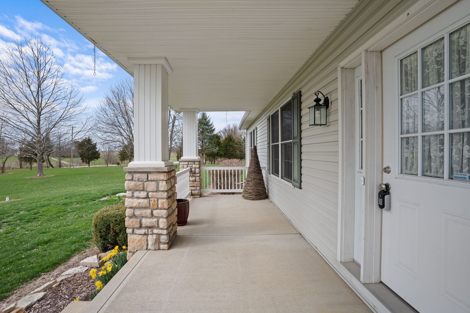 Covered front porch with stone columns, white trim, and a lush green lawn view on a cloudy day.