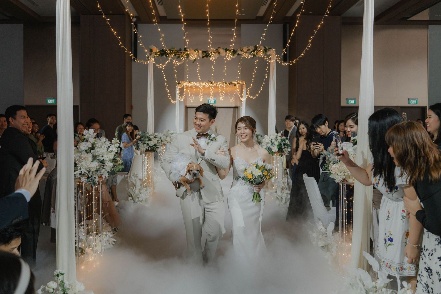 Wedding guests dance and celebrate under elegant crystal chandeliers at an indoor reception venue.