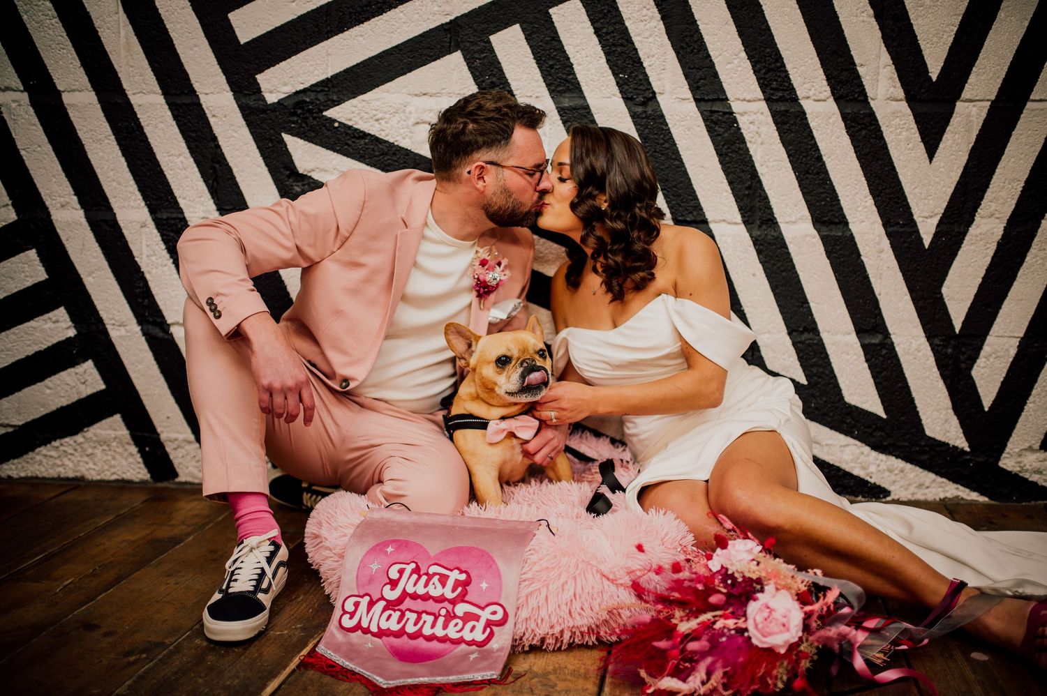 Wedding couple and guests enjoy a fun moment together against a black and white striped backdrop.