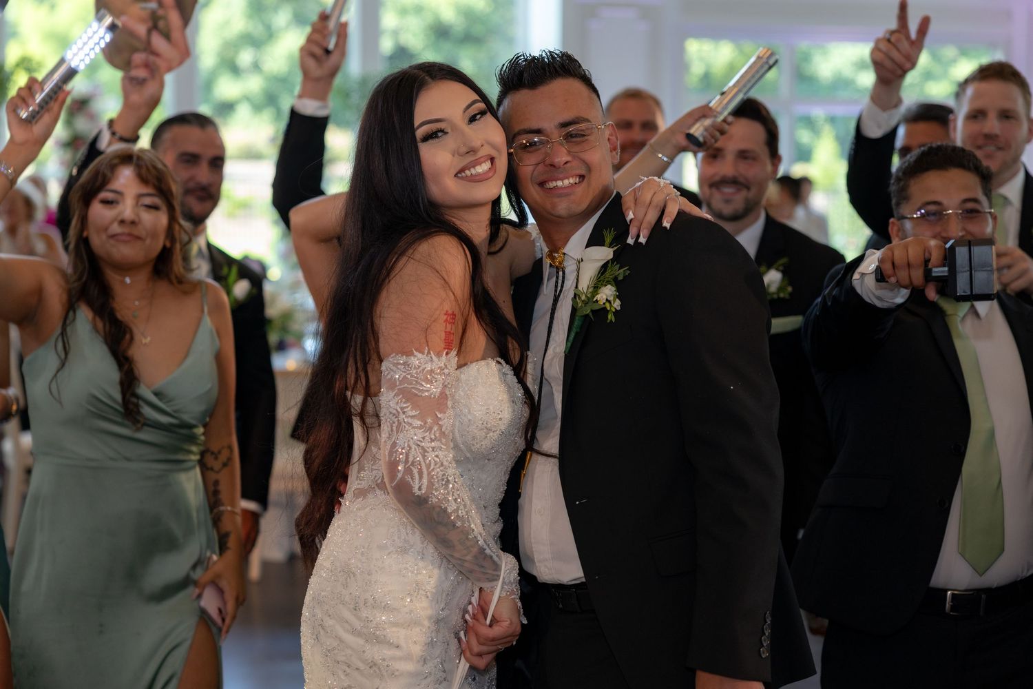 A group of wedding guests dancing and celebrating together at a reception with raised hands and joyful expressions.
