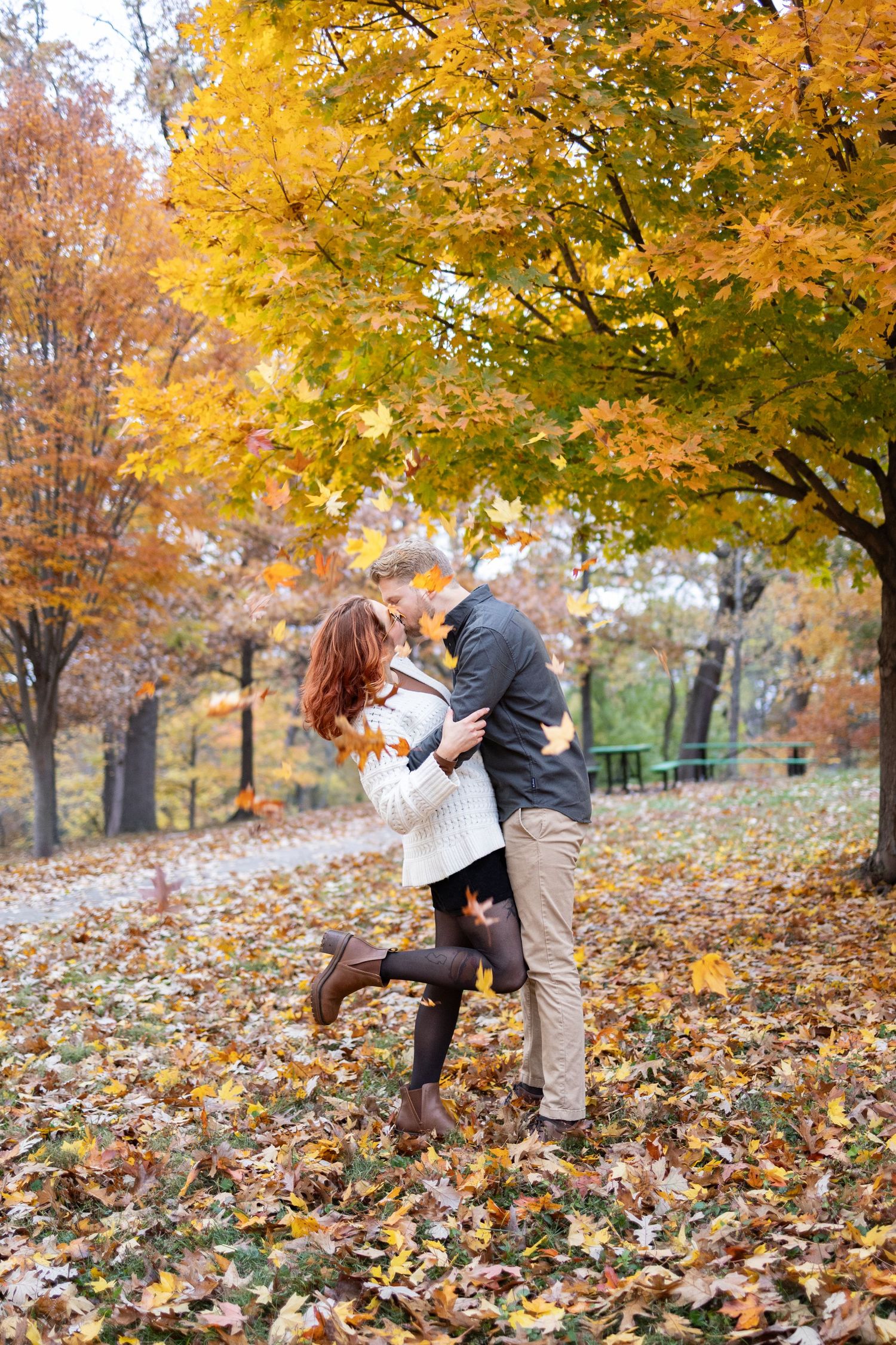 Couple sharing a romantic kiss in an Eden Park surrounded by vibrant yellow and orange fallen leaves.