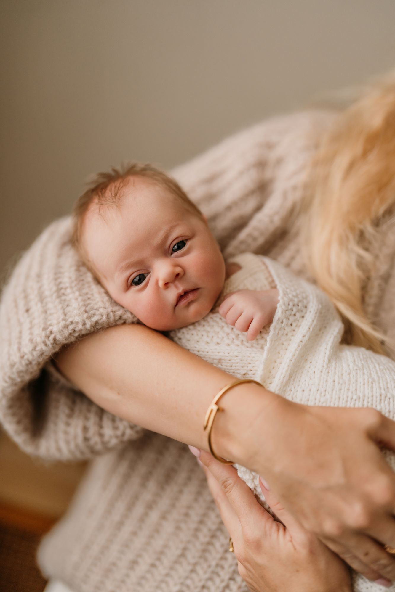 A newborn baby resting on a mother's arm, wearing a white knit outfit