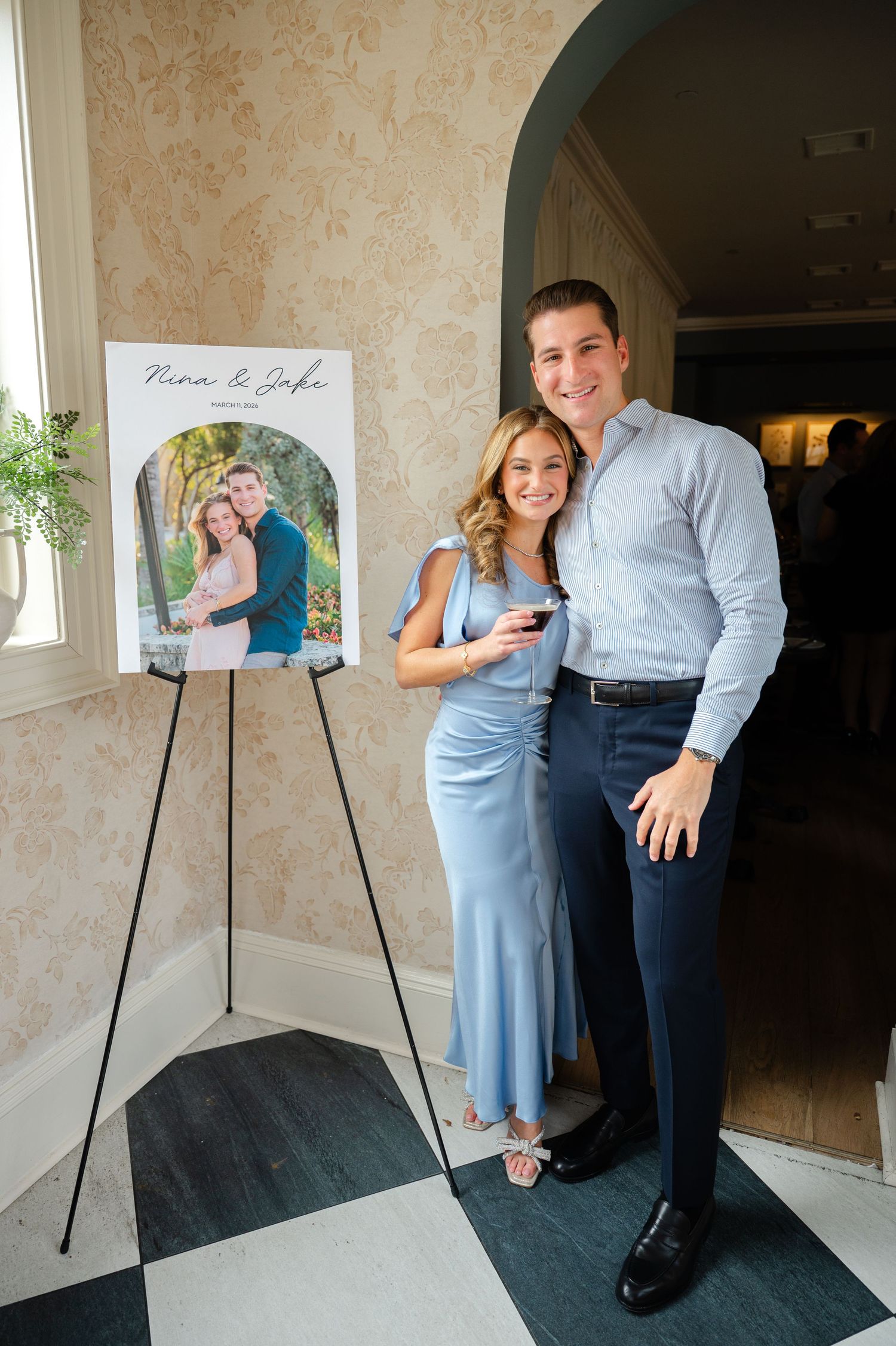 Couple kissing beside an engagement photo display sign at their celebration event in an elegant venue.