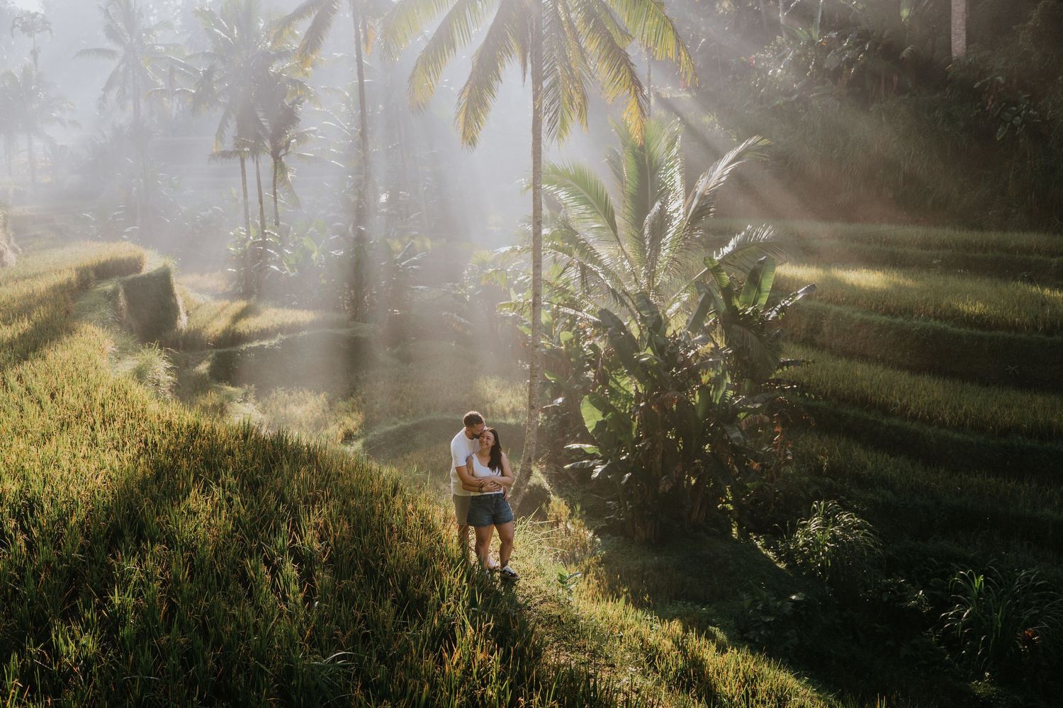 Couple walking along a green garden pathway surrounded by tropical plants.